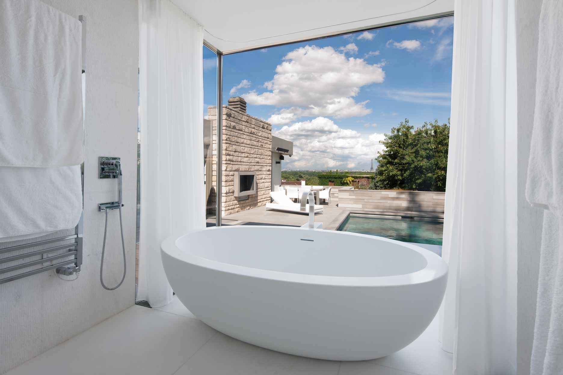 Baignoire dans une salle de bain avec vue sur une terrasse extérieure et un ciel bleu avec des nuages