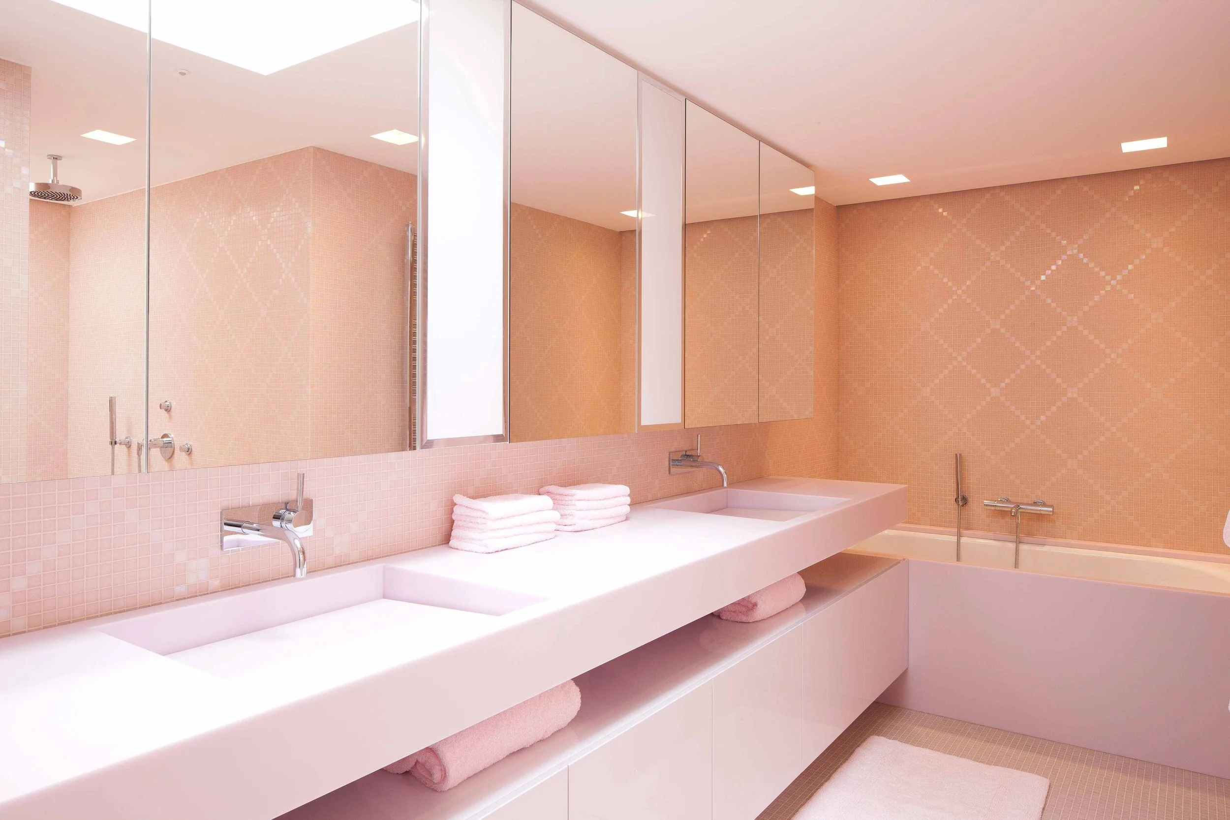 Salle de bain avec double lavabo blanc, miroirs, baignoire avec robinetterie, serviettes blanches et rose, murs en carrelage rose, sol en mosaïque beige