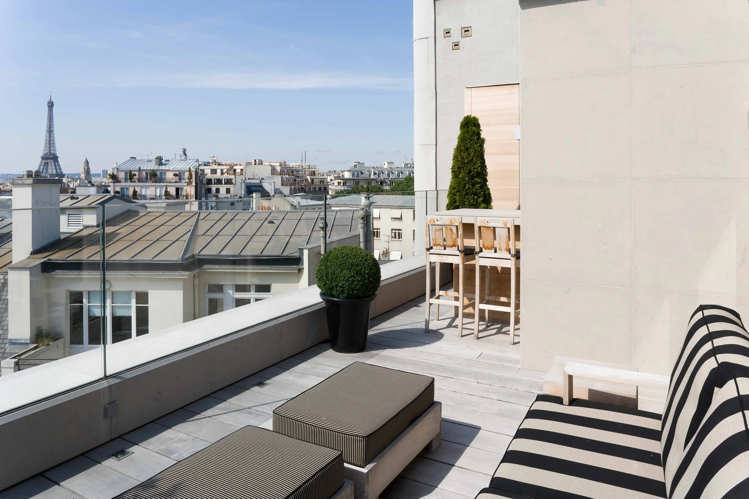 Balcon avec mobilier urbain, plantes en pot, vue sur Paris et la Tour Eiffel au loin.