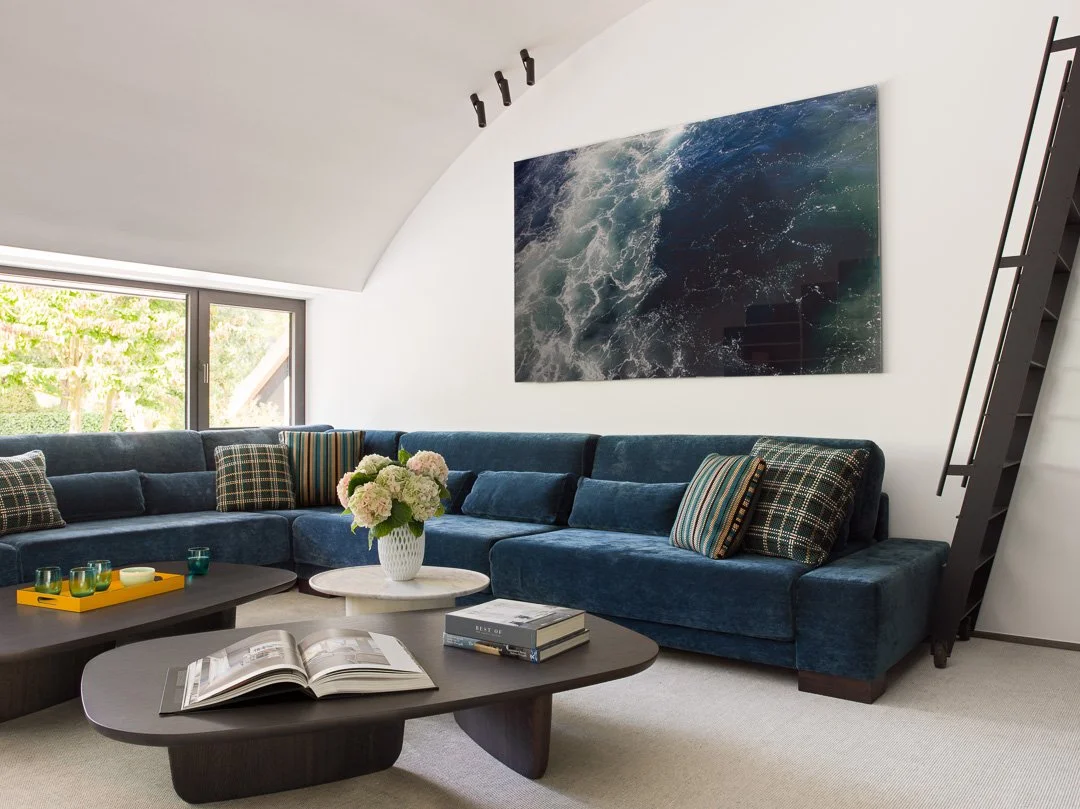 Salon moderne avec canapé bleu, table basse, peinture représentant des vagues, et escalier en métal.