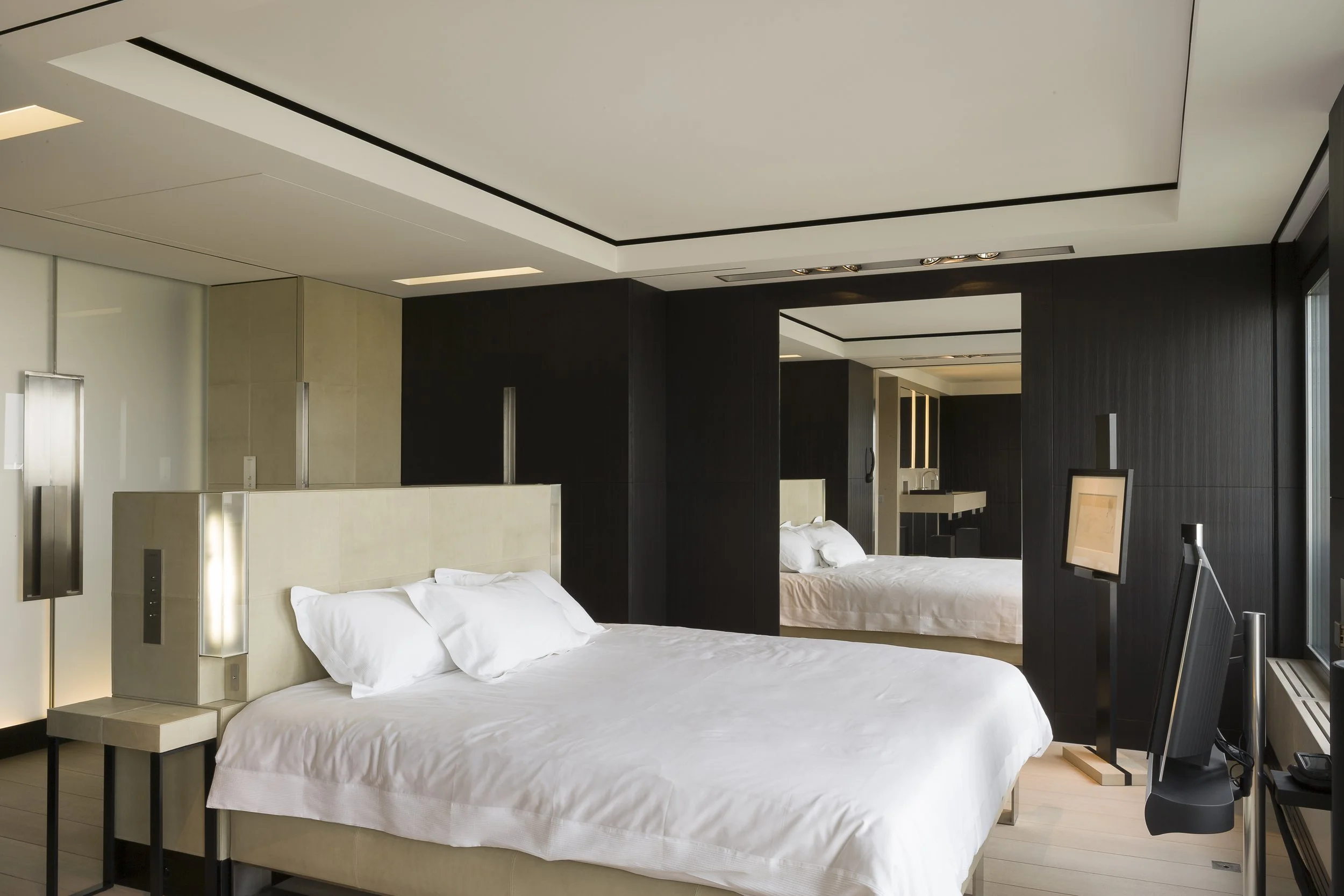 Chambre d'hôtel moderne avec lit king-size, éclairage intégré et écrans de télévision.