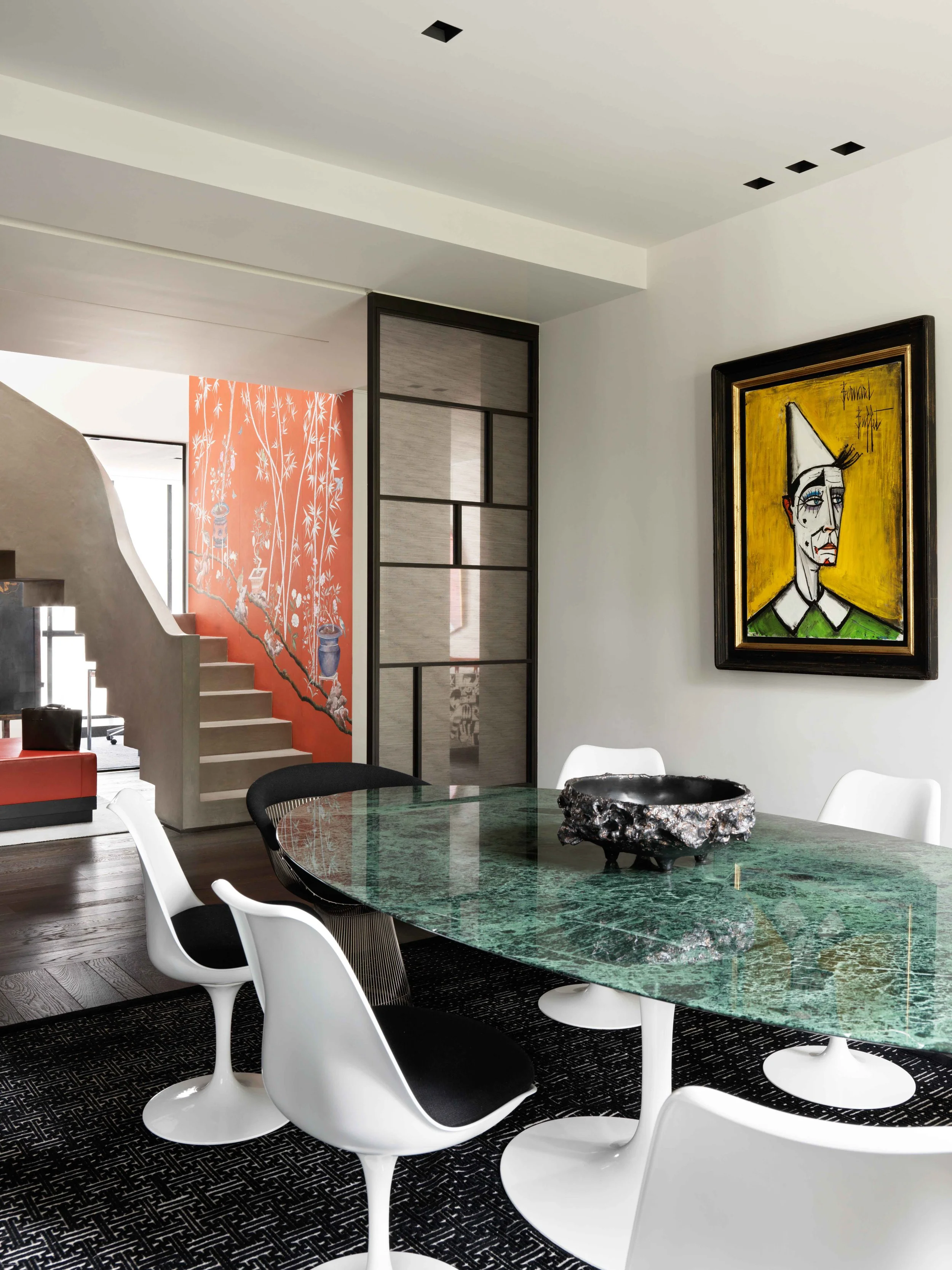 Une salle à manger moderne avec une table en marbre vert, des chaises blanches et noires, un tableau de style cubiste accroché au mur, et une décoration intérieure élégante.