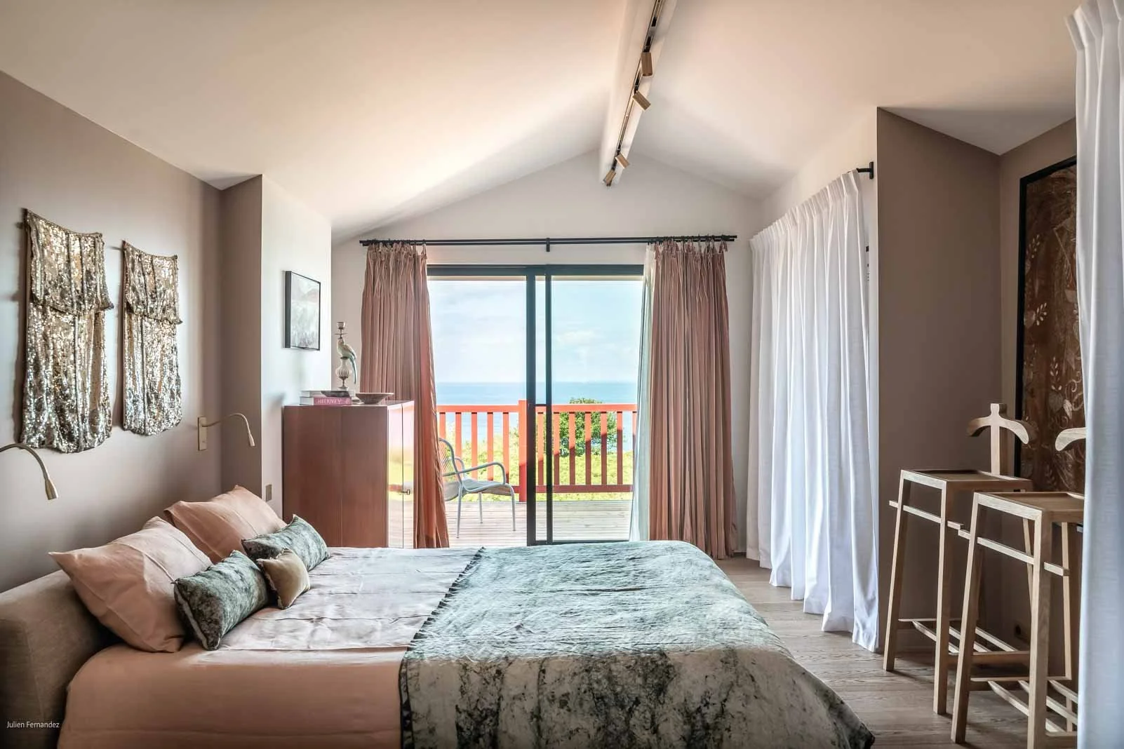 Chambre avec lit, fenêtres avec draps blancs et rideaux roses, vue sur l'océan depuis le balcon, décoration moderne.