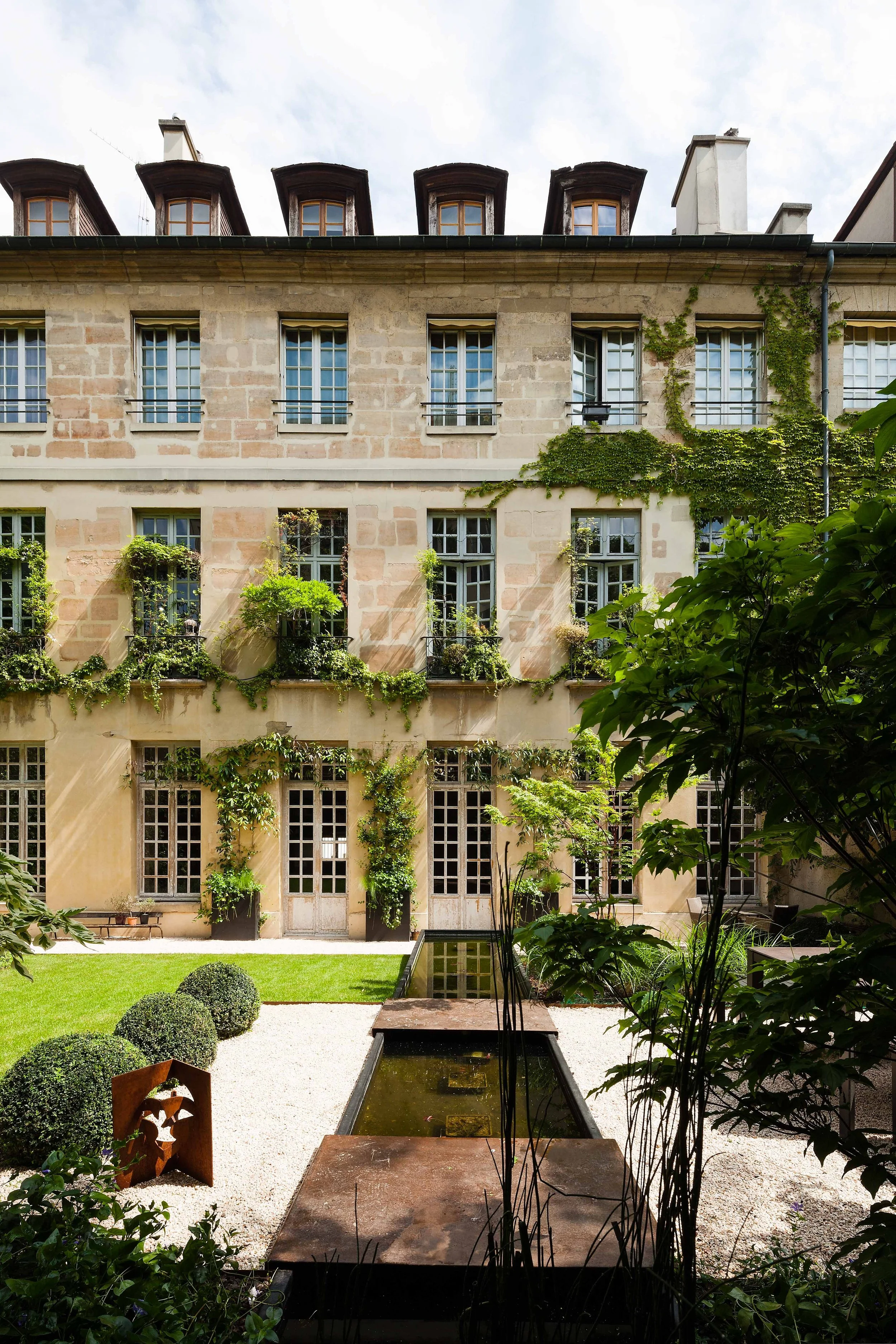 Cour intérieure d'un bâtiment ancien avec jardin, plantes grimpantes et bassin au centre.