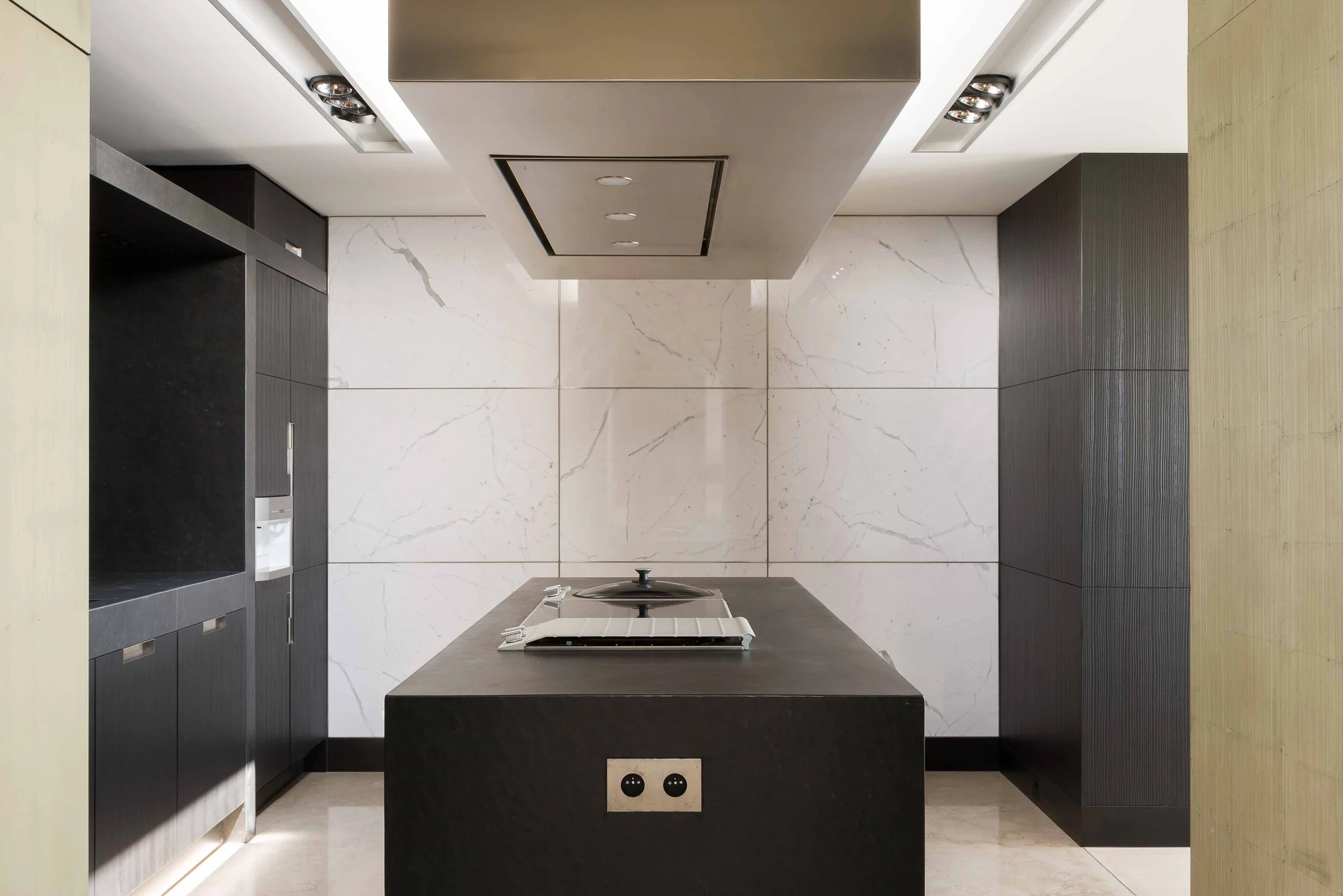 Cuisine moderne avec un plan de travail noir, panneau en marbre blanc derrière et un plafonnier en haut.