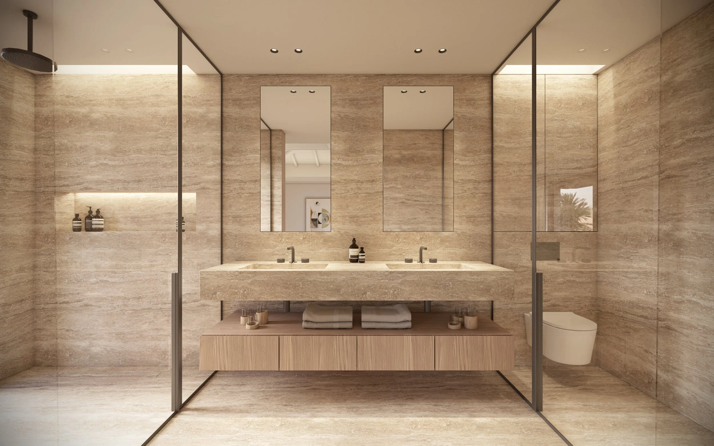 Salle de bain moderne avec murs et sol en pierre beige, double lavabo, grands miroirs, sèche-serviettes, et WC suspendu visible à travers une cloison de verre.