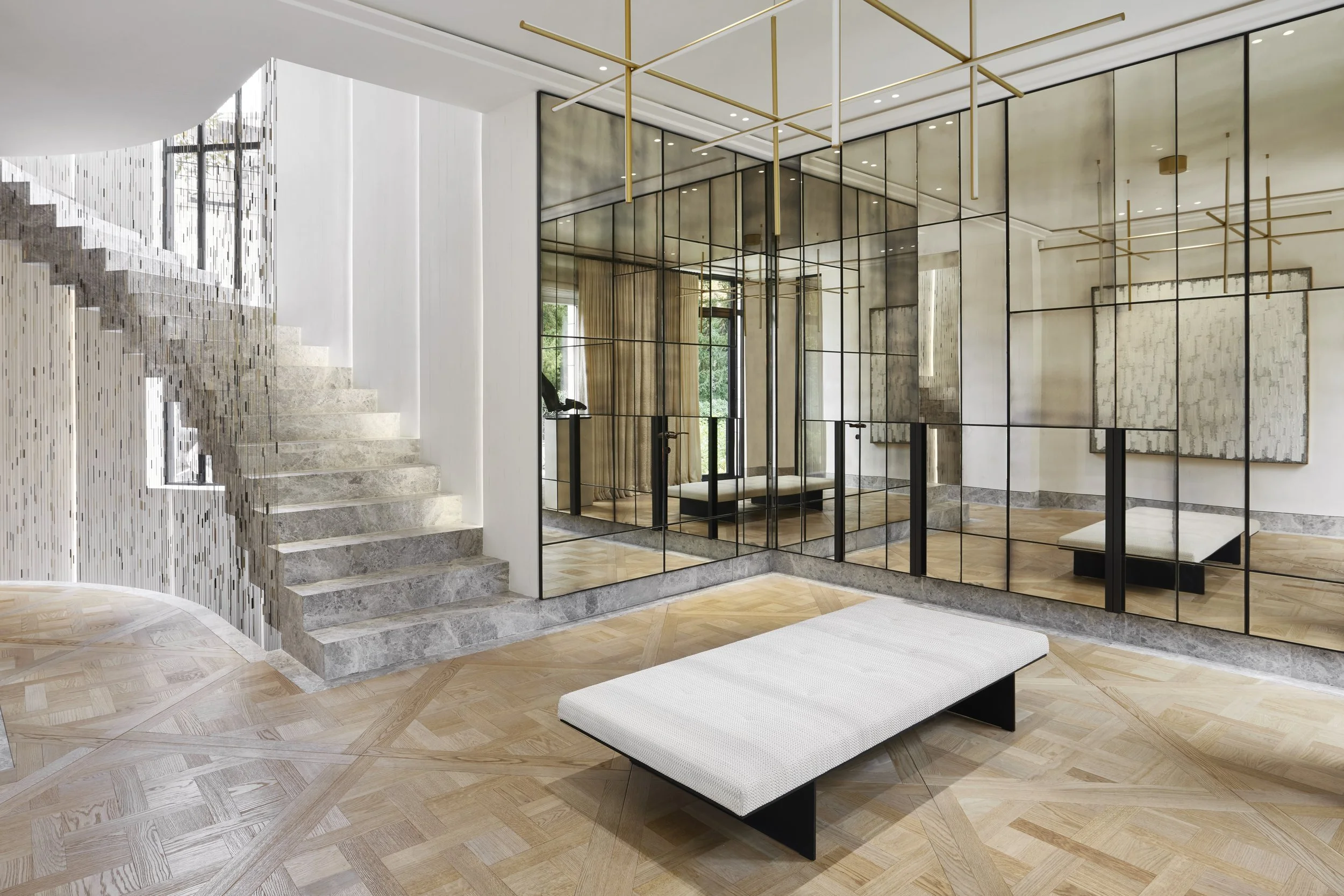 Intérieur contemporain avec escalier en pierre, mur en miroir créé avec une structure métallique noire, grandes fenêtres avec rideaux en tissu beige, plancher en bois clair, et un banc blanc