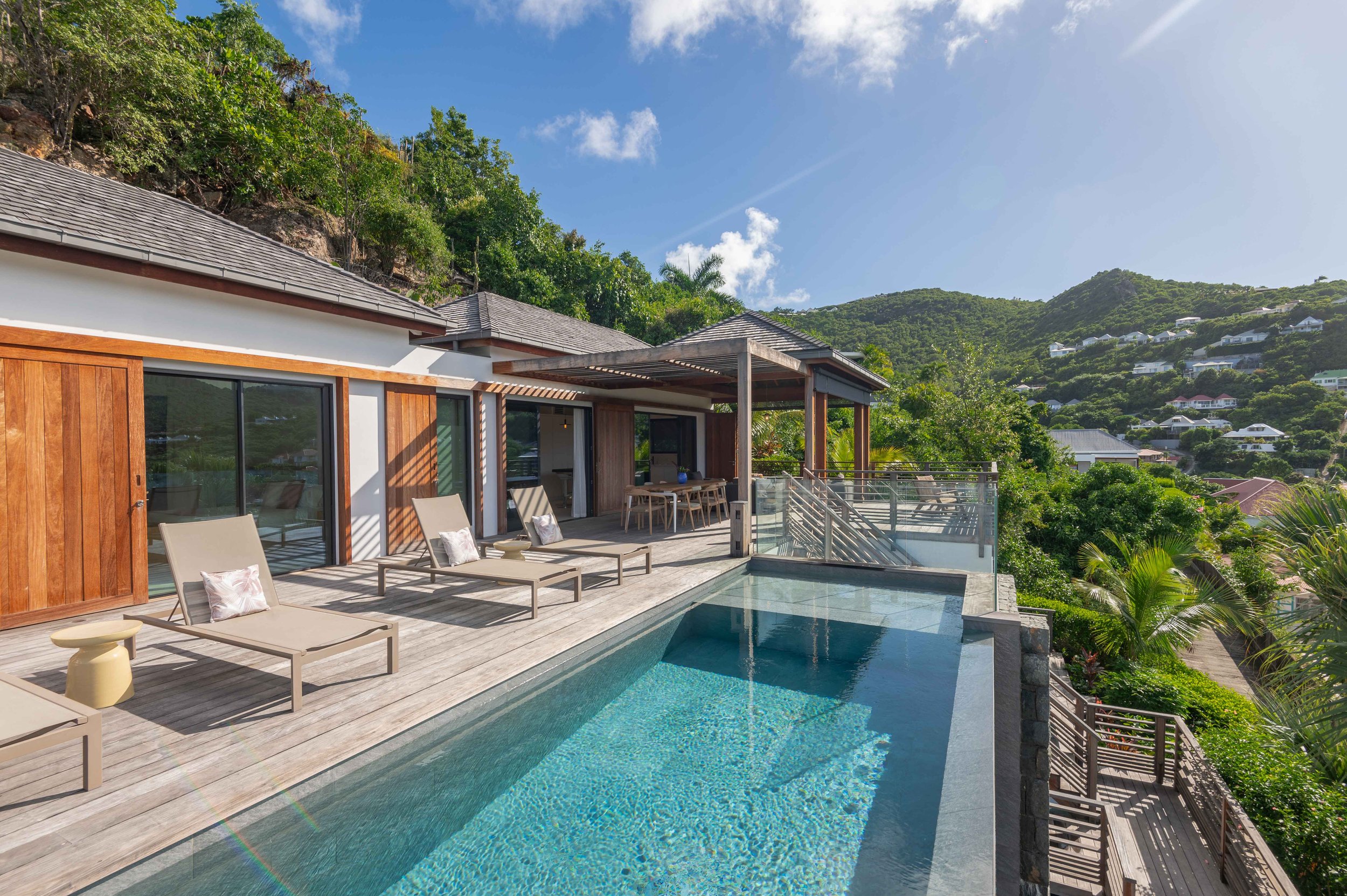 Terrasse avec piscine, chaises longues et vue sur une colline verte avec des maisons