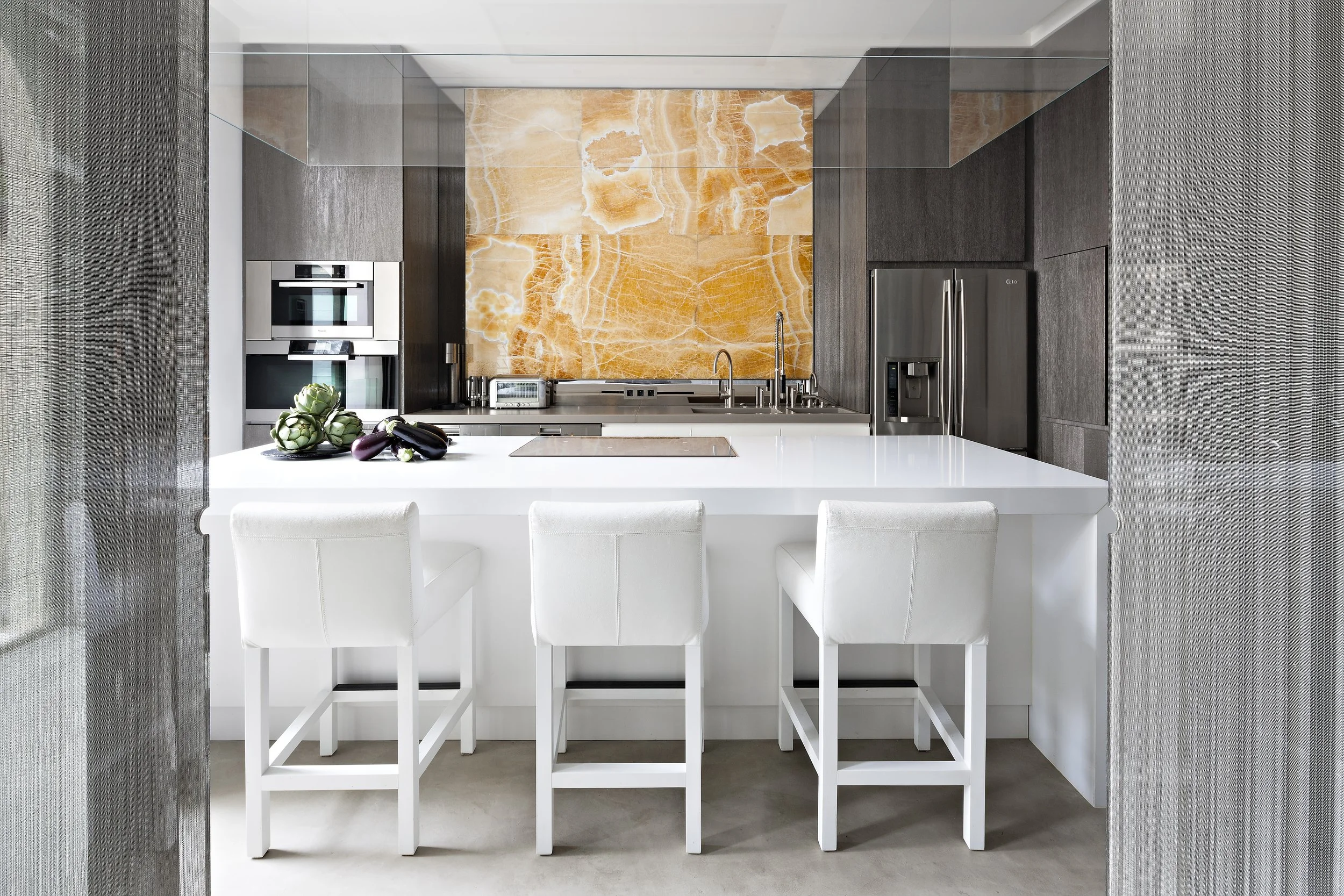 Cuisine moderne avec îlot blanc, trois chaises blanches, murs en bois foncé, arrière-plan avec une grande pierre orange