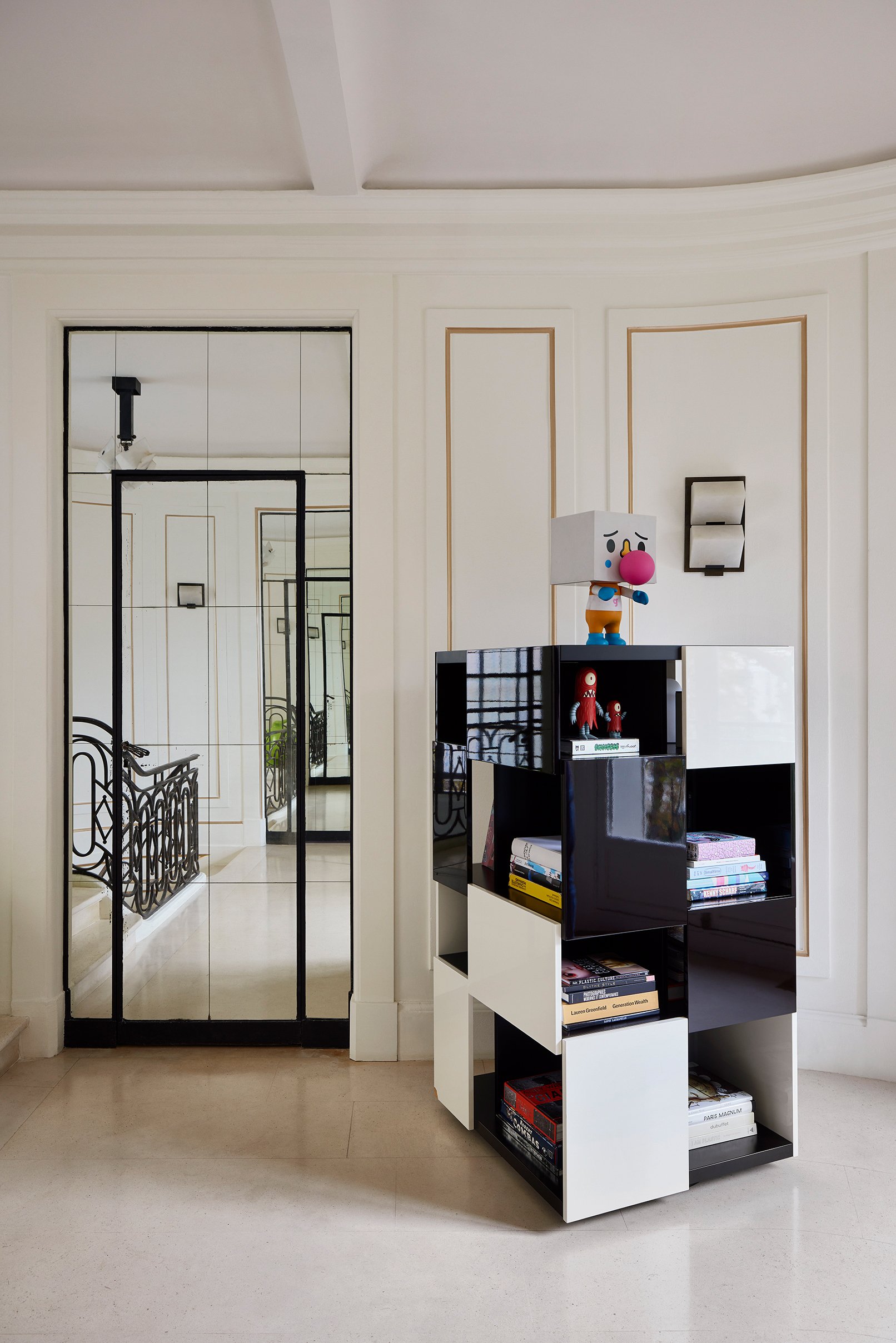 Intérieur moderne avec un mur blanc, un miroir en verre, une étagère noire et blanche avec des jouets en haut, dont un personnage avec un gros nez rose.