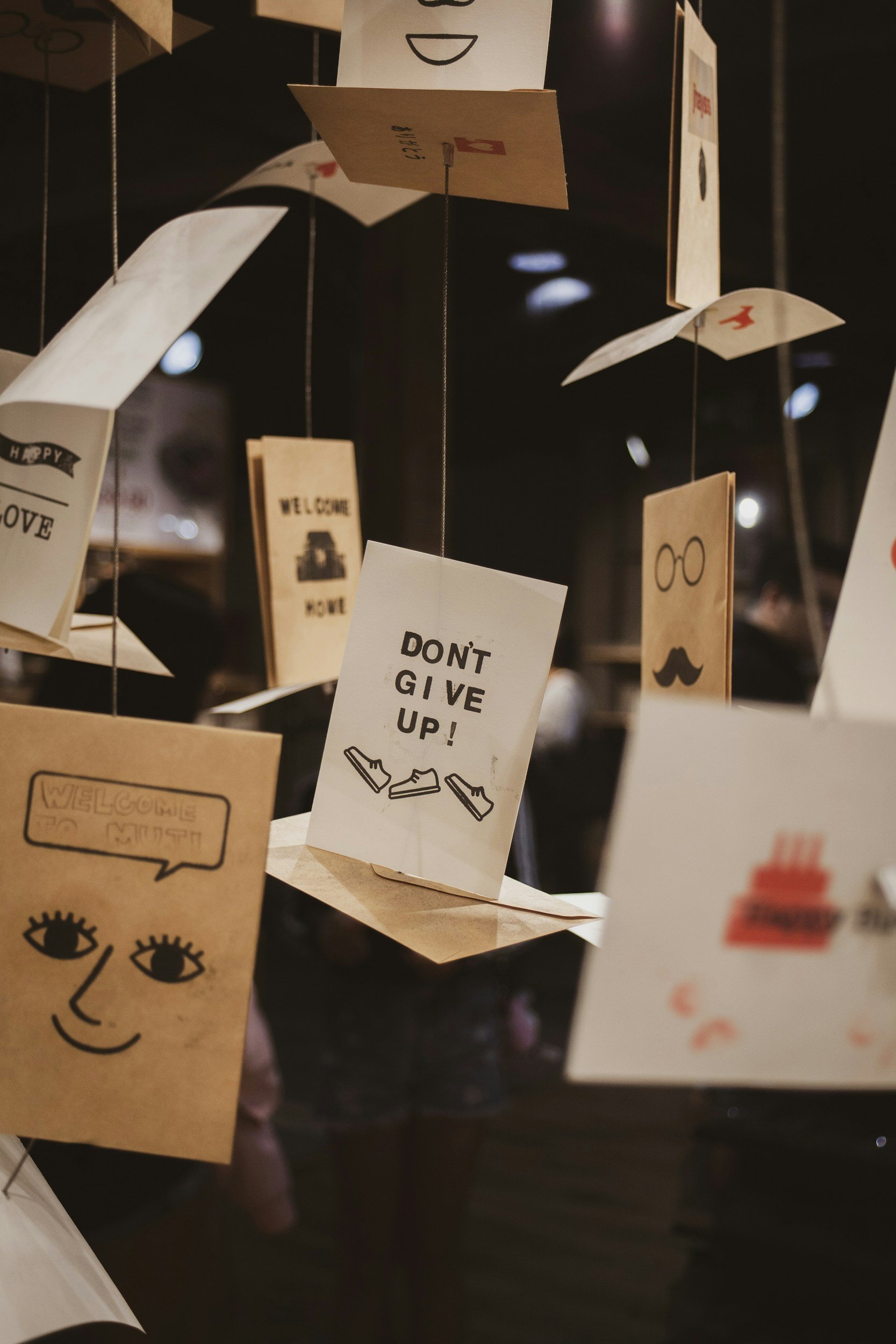 Various paper cards with illustrations and messages hanging on strings, including one reading 'DON'T GIVE UP!' and with welcome, and decorative elements.