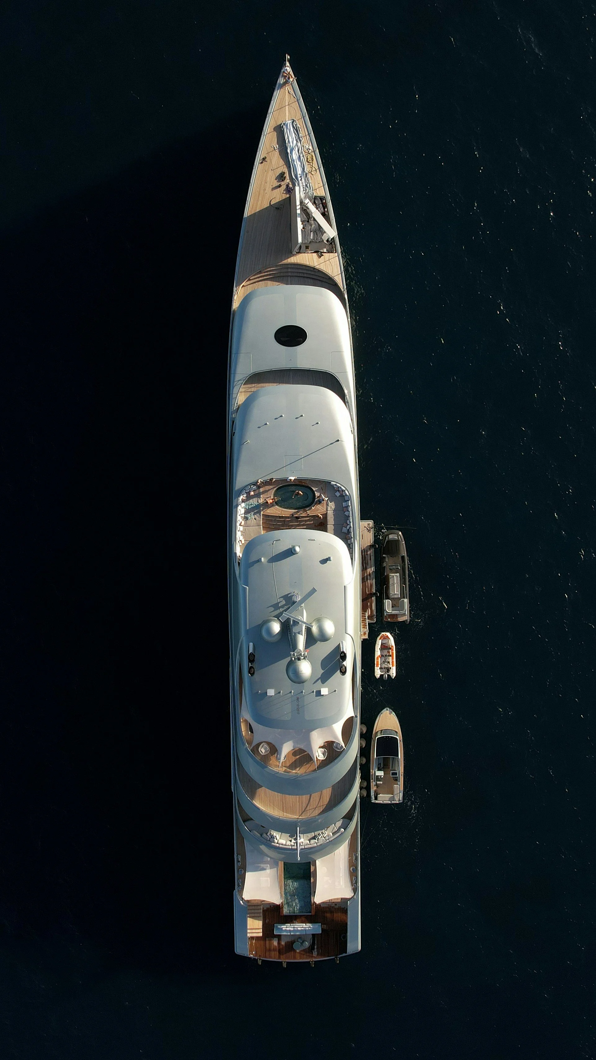 Aerial view of a luxury yacht with multiple smaller boats docked alongside it, floating on dark blue water.