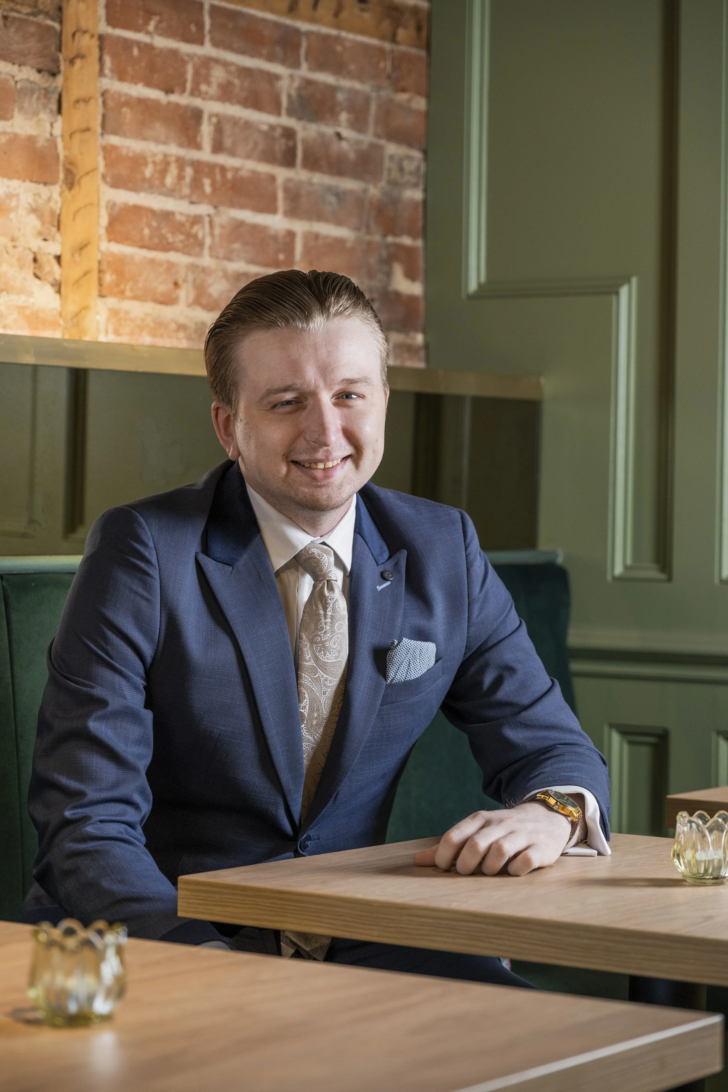 Andreas in a blue suit and cream patterned tie sitting at a table in the Old Town Bistro,  a modern restaurant with brick and green-paneled walls.