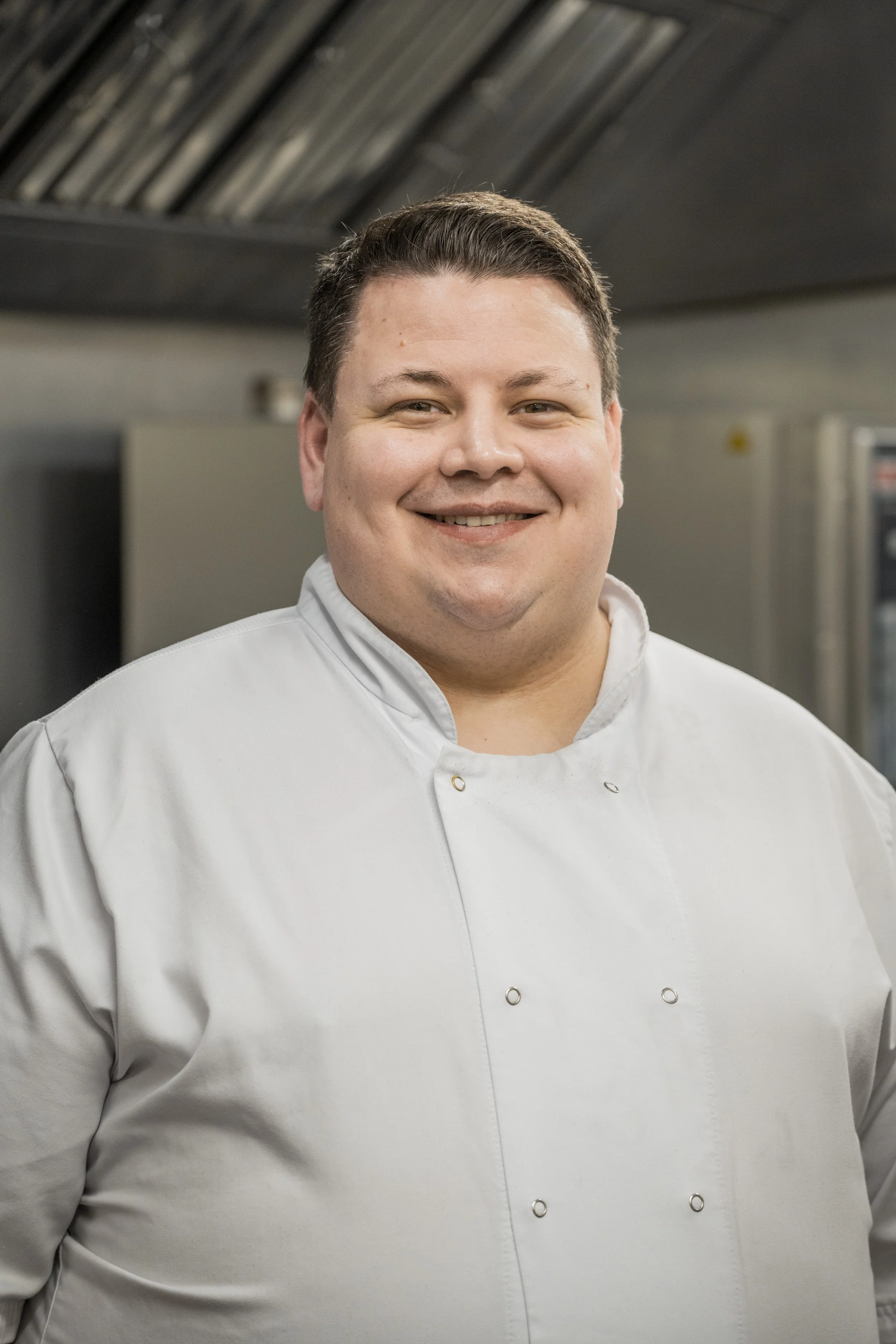 Chris, wearing his chef whites smiling in the Old Town Bistro's professional kitchen.