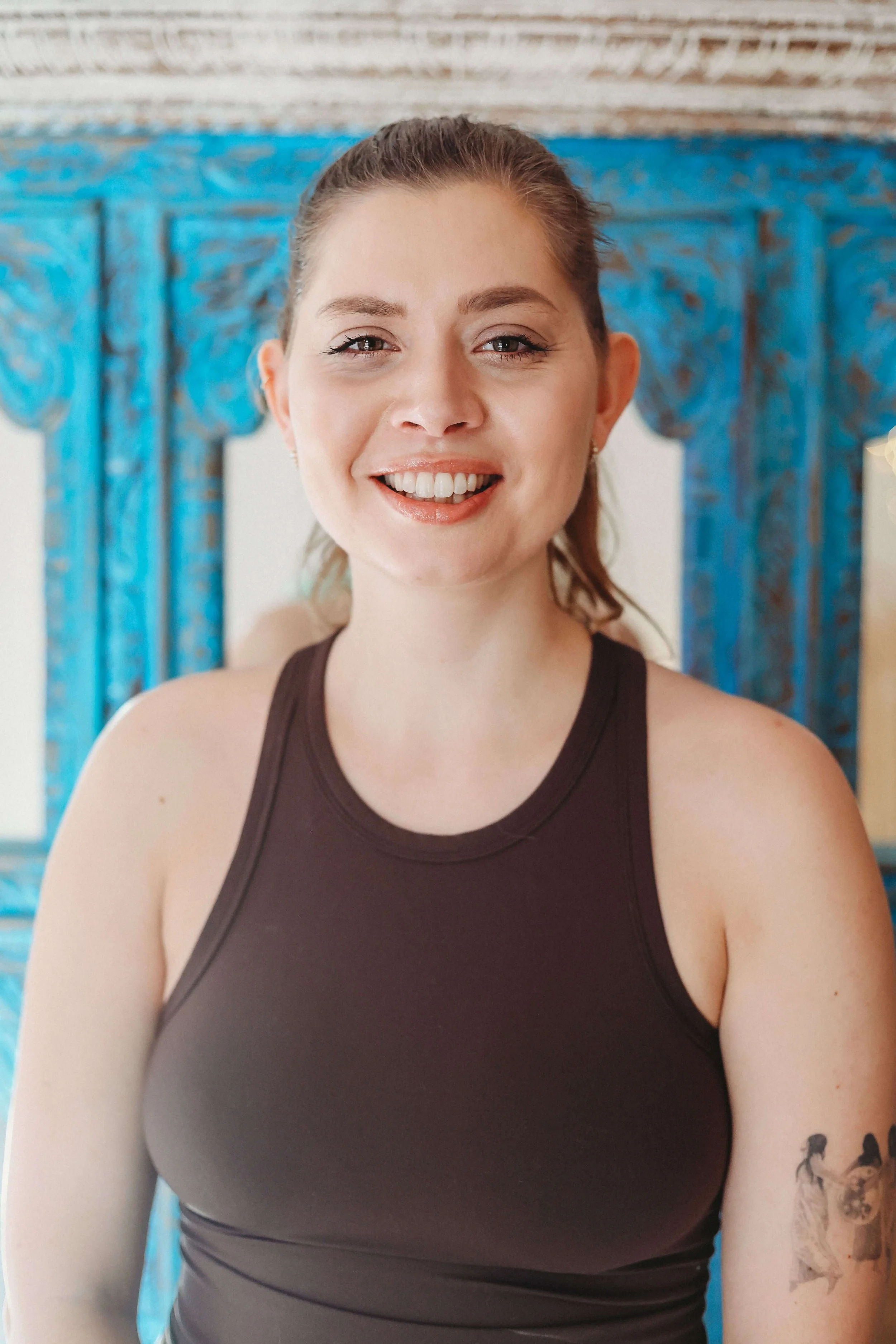 A yoga teacher in a brown vest top with a spiritual arm tattoo, at Yomi yoga studio in Market Harborough, Leicestershire