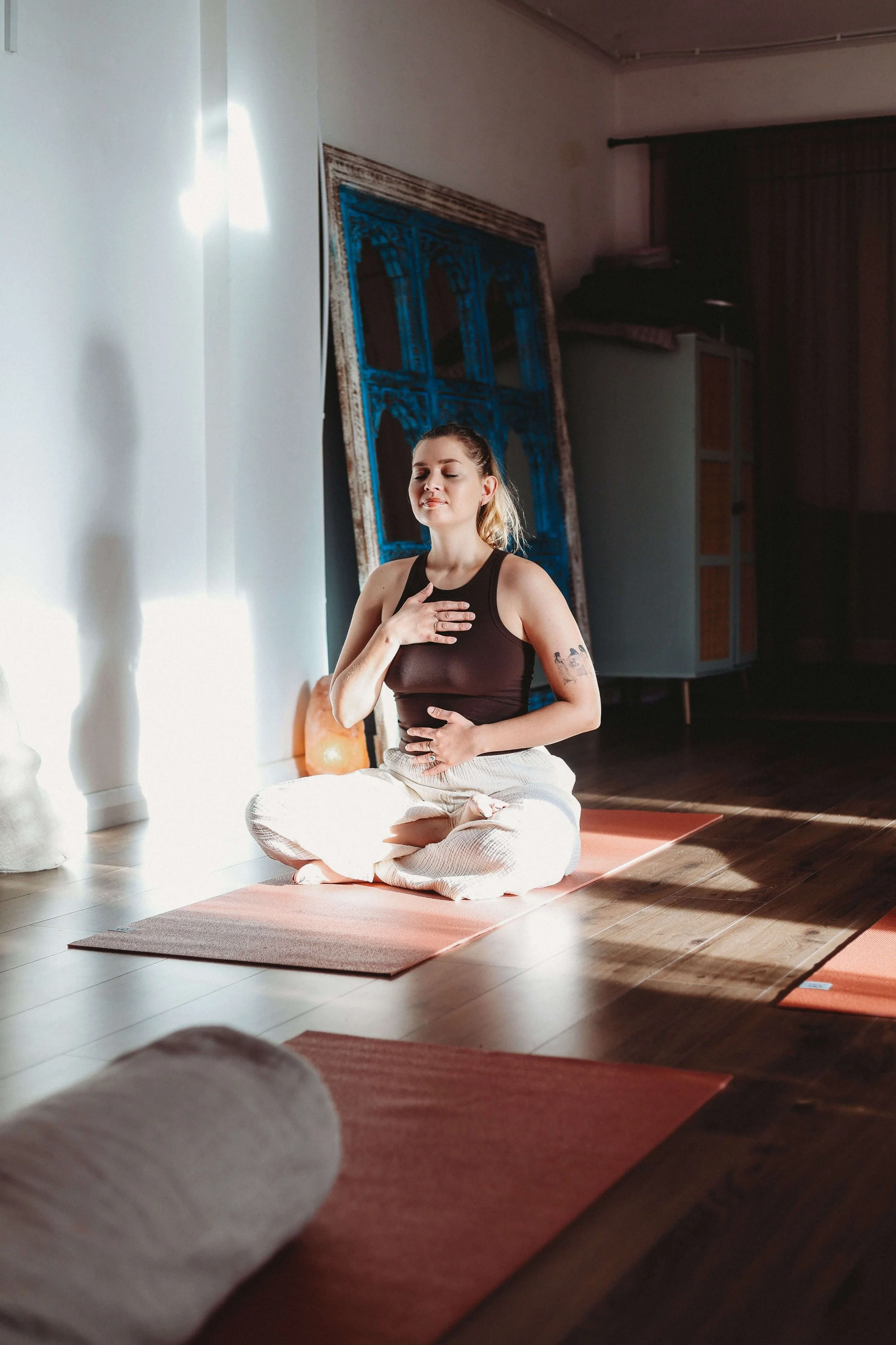A woman in a brown vest top and cream wide leg trousers with eyes closed doing meditation and breathwork at Yomi yoga studio in Market Harborough, Leicestershire