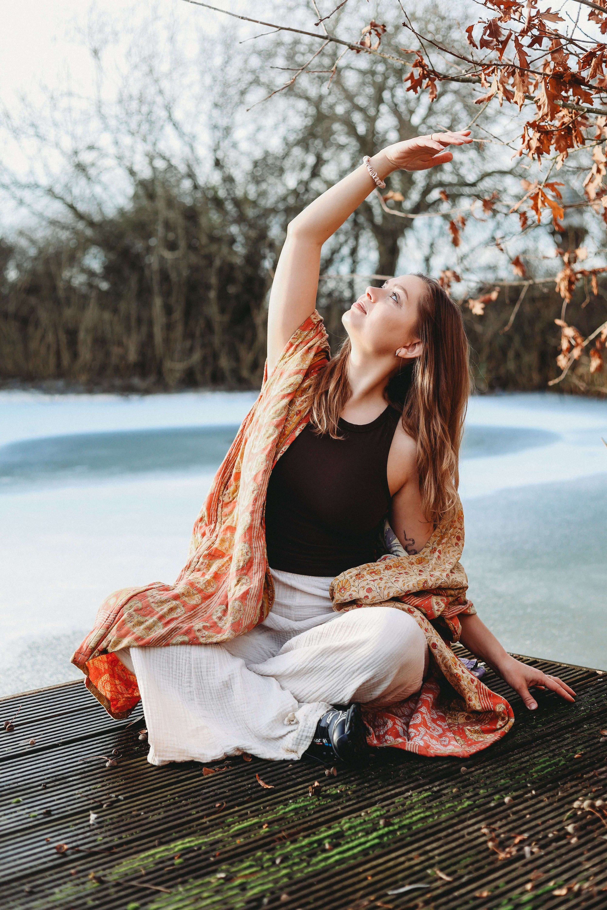 A woman in an orange kaftan practices yoga in nature with a gentle side stretch in Market Harborough