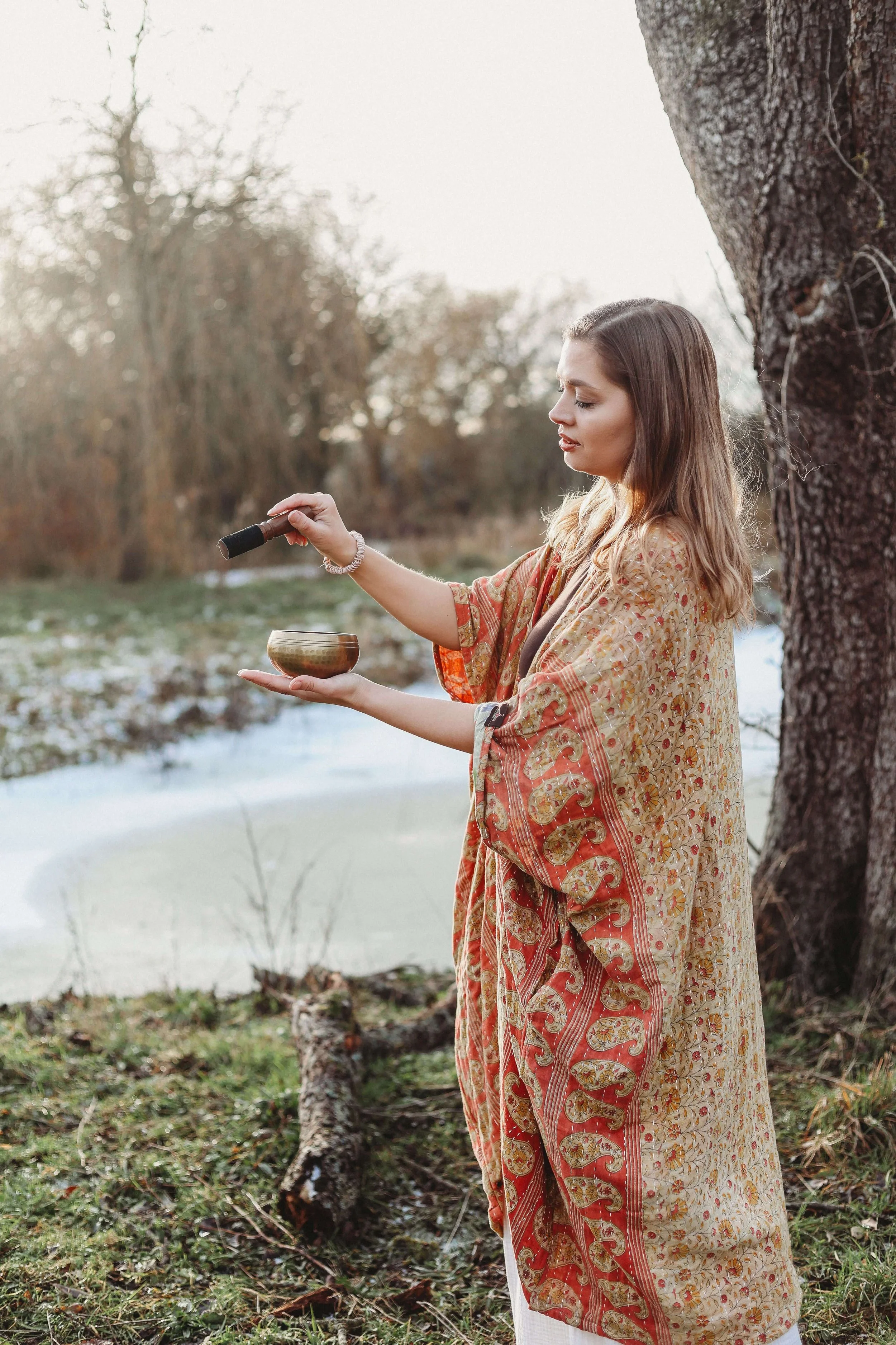 A woman in an orange kaftan is using a sound bowl and meditating in nature in Market Harborough, Leicestershire