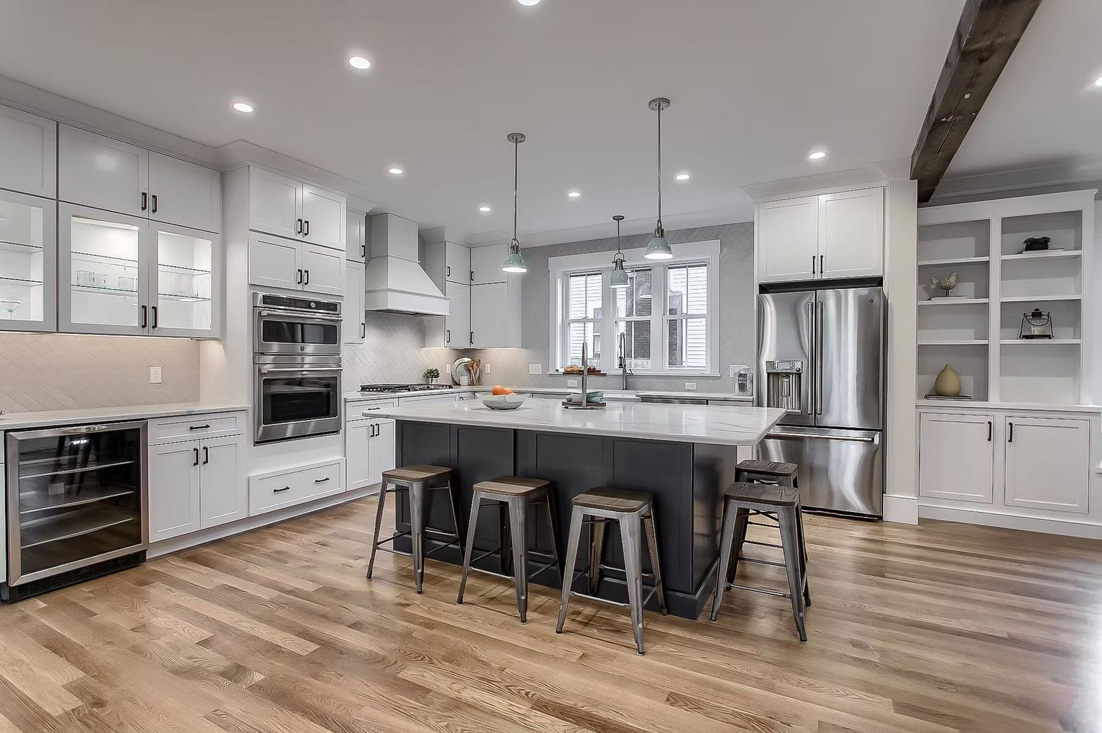 Modern kitchen with white cabinets, stainless steel appliances, a black kitchen island with stools, hardwood floors, and pendant lighting.