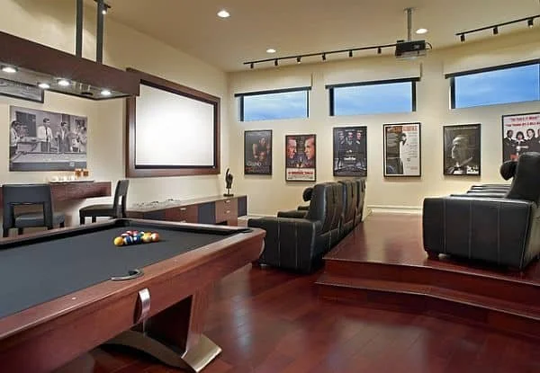 A home theater room with a pool table, black leather recliners, and framed posters on the walls.