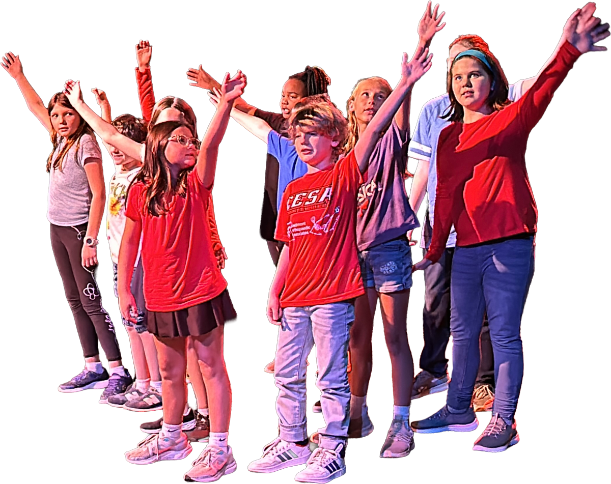 A group of children performing on stage with arms raised, some with serious expressions, under colorful stage lighting.