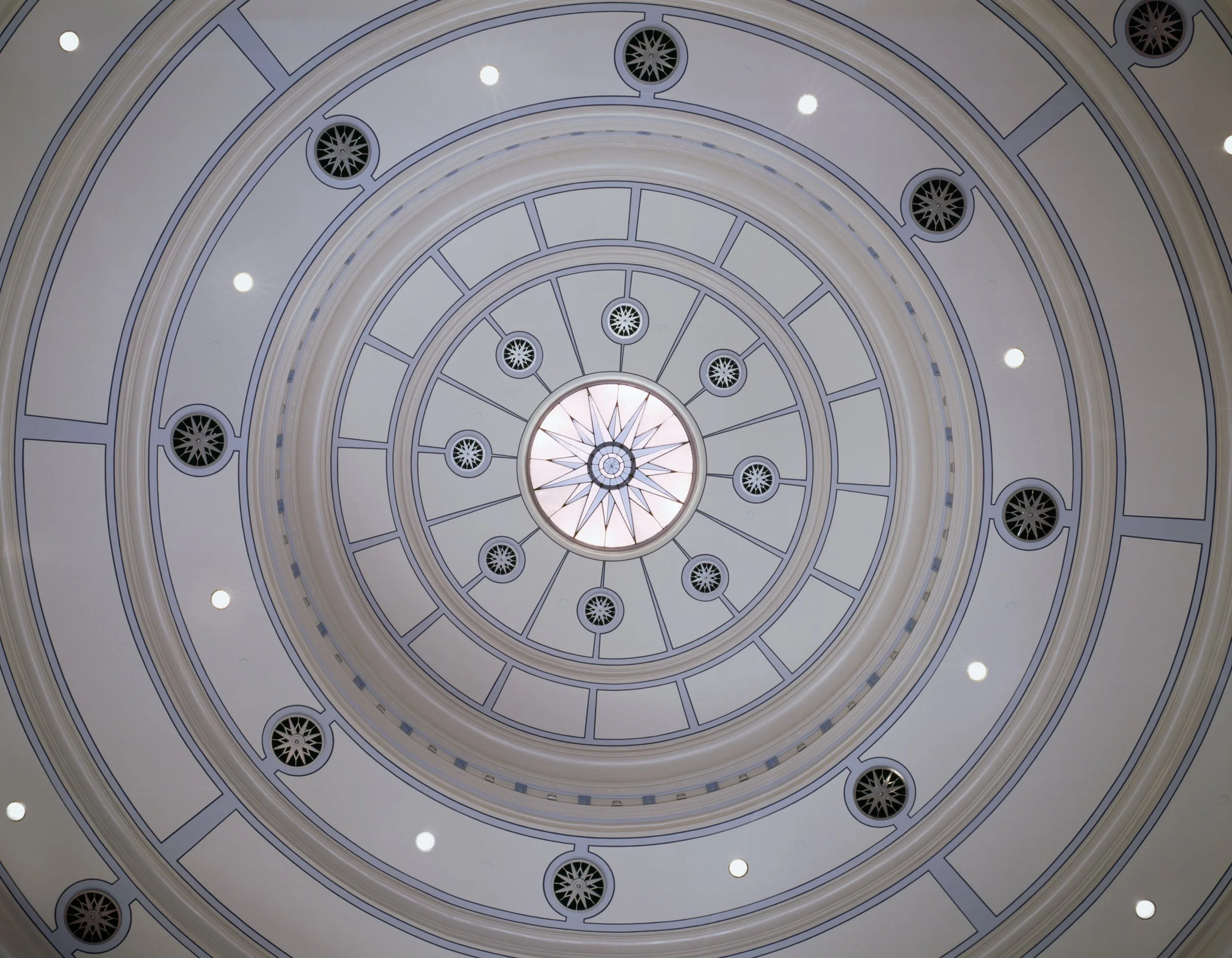 Interior view of a domed ceiling with concentric circular patterns, decorative vents, and small round lights.