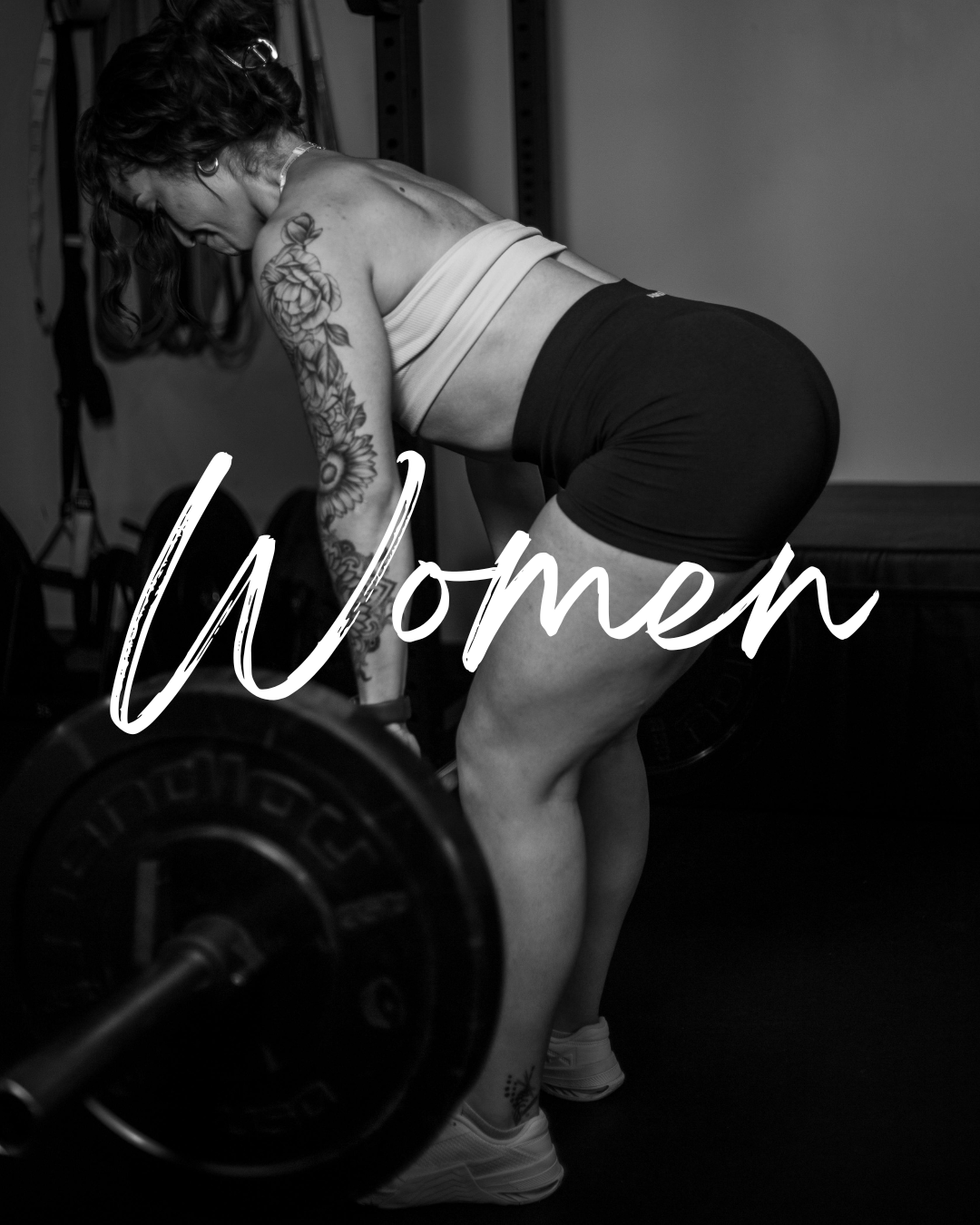 Black and white photo of a woman with tattoos performing a deadlift in a gym, with the word 'Women' written across the image.