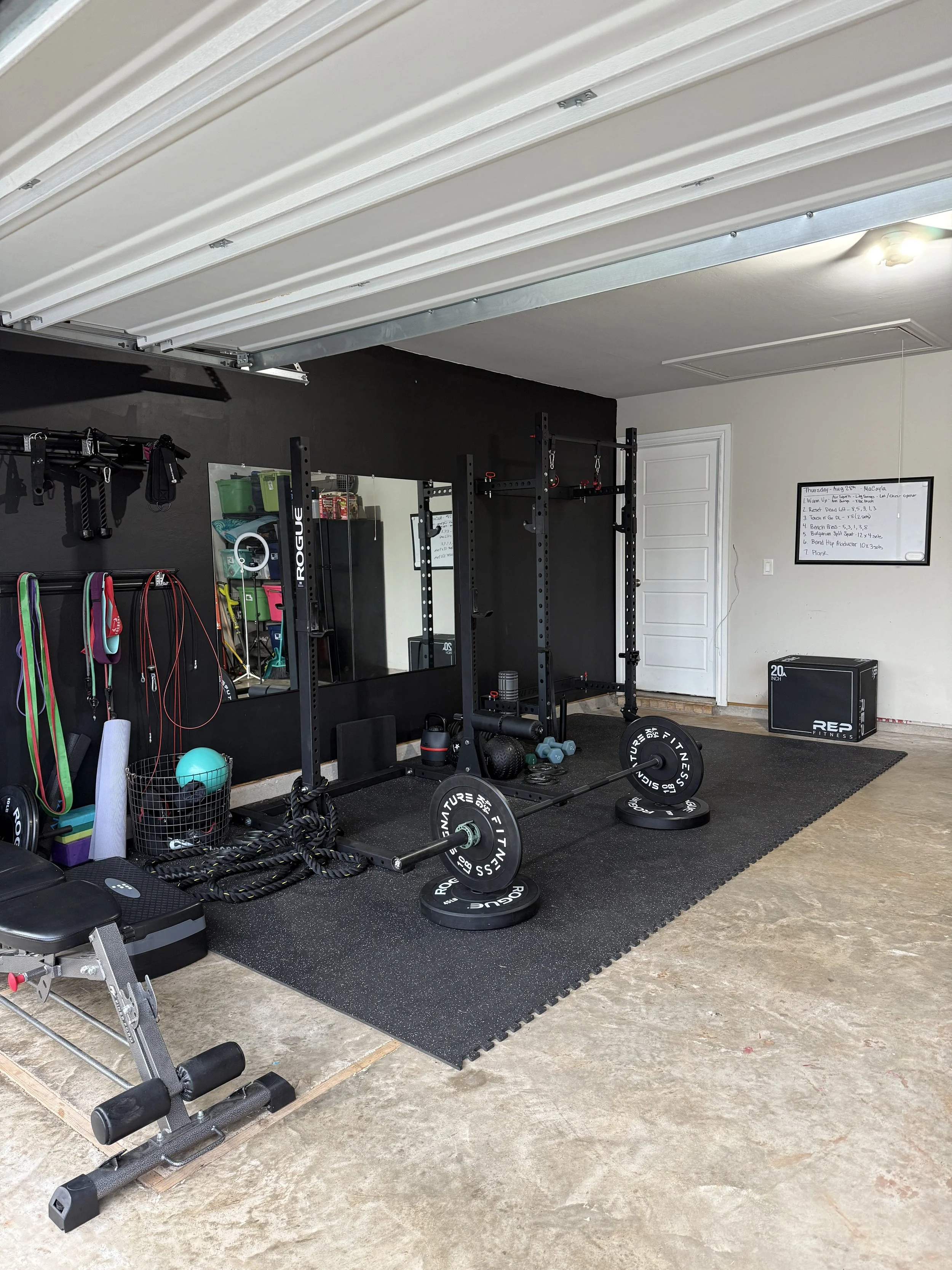 Home gym with weightlifting equipment, medicine balls, resistance bands, and a whiteboard with workout notes.