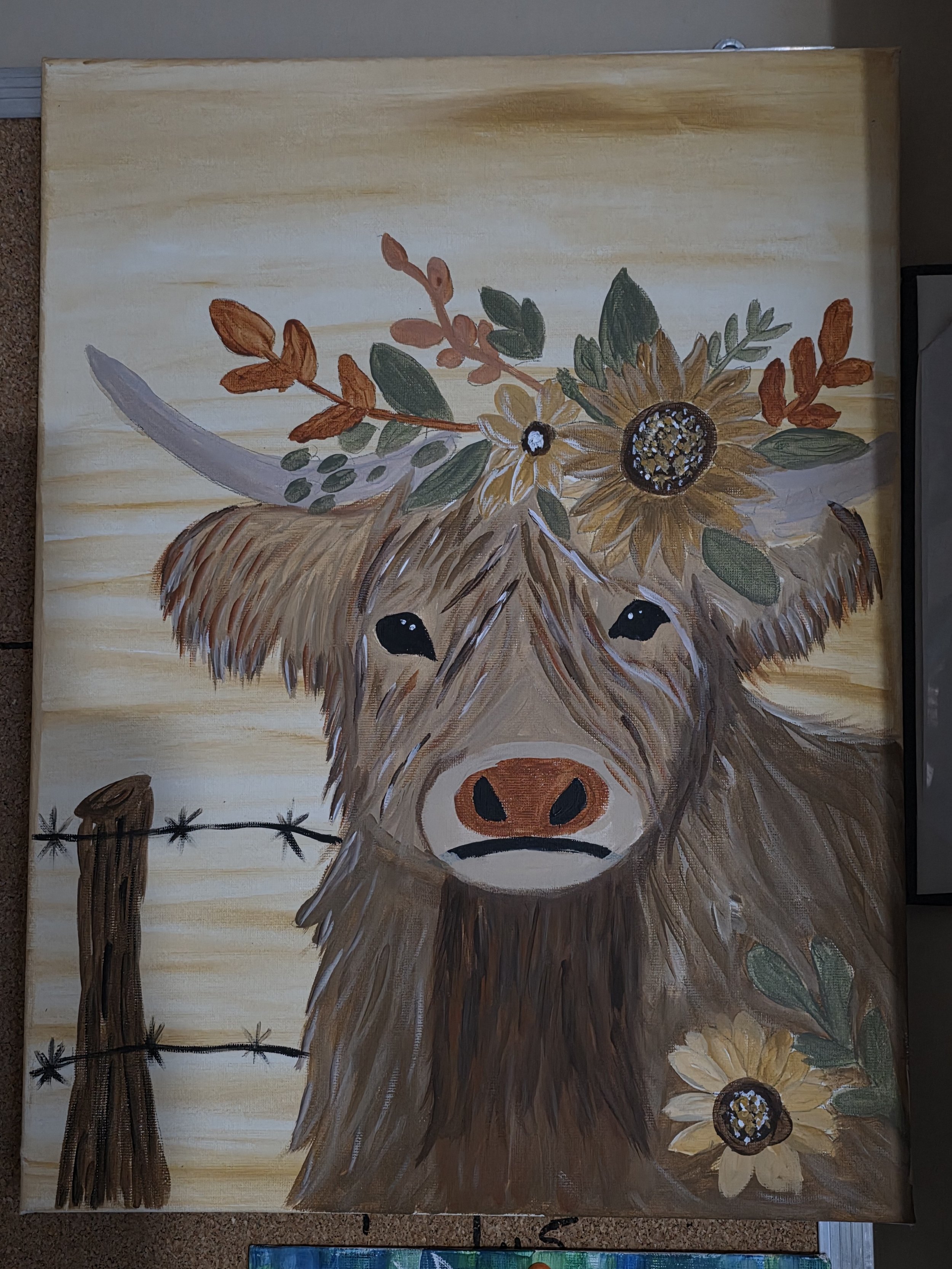 Painted portrait of a Highland cow with a floral crown featuring sunflowers and leaves. The background includes a barbed wire fence.