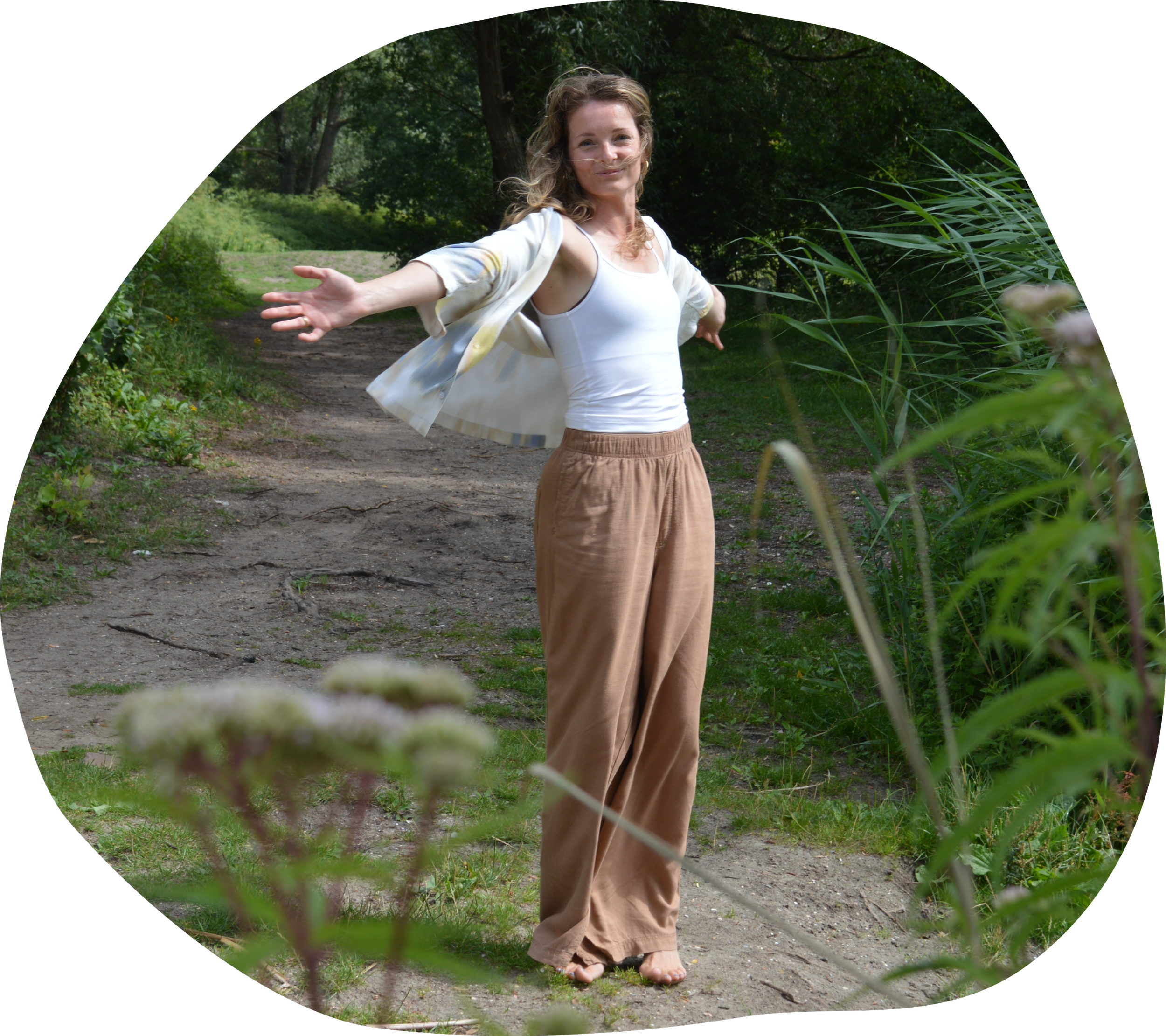 Nadia van Wylde Roots met open armen die op een bospad loopt, groene bomen en planten op de achtergrond.