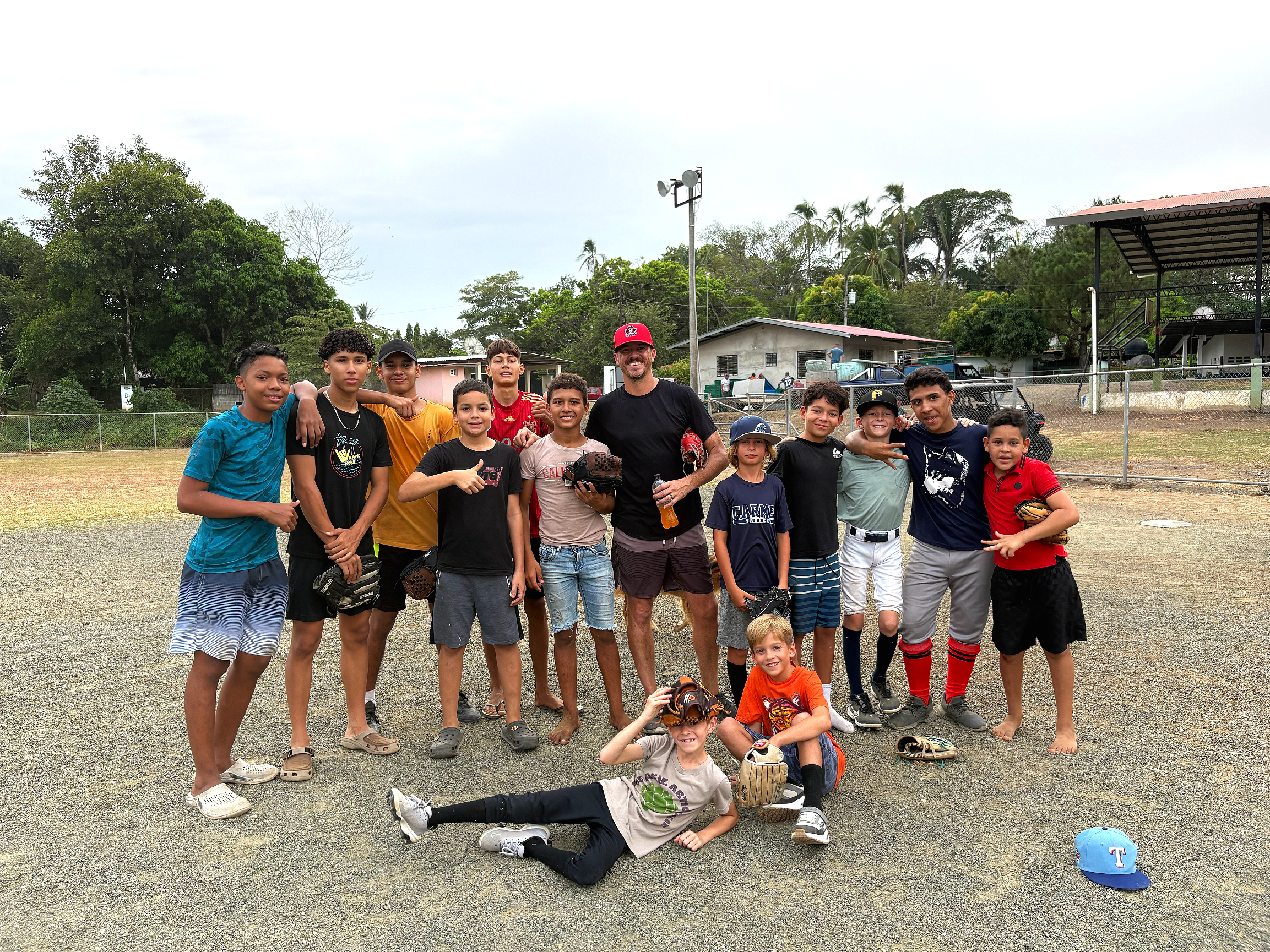 Group of children and a coach on a baseball field posing for a photo, some holding baseball gloves.