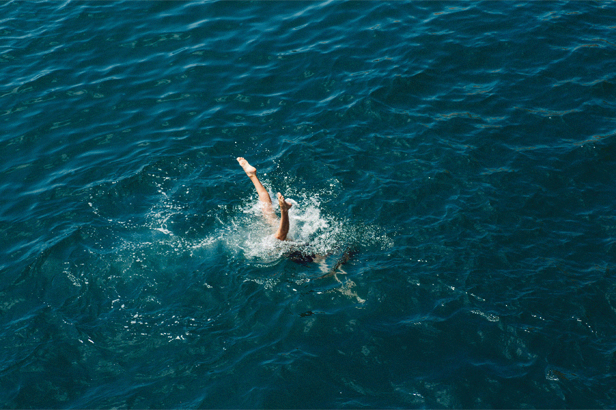 Eine Person, die im Wasser taucht, nur die Beine sind sichtbar, das Wasser ist blau und klares Meer.