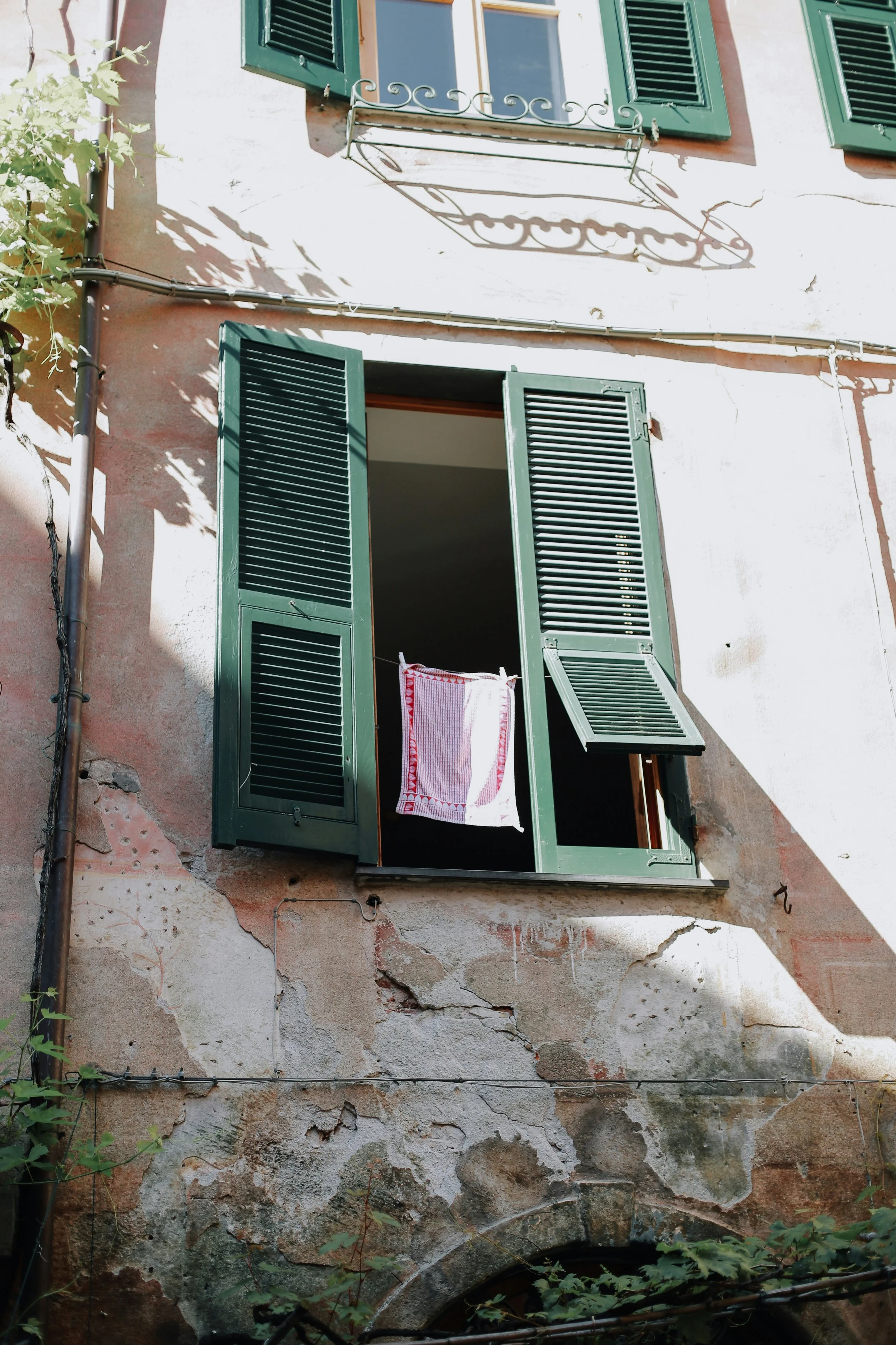 Ein altes, durch Wetter und Zeit beschädigtes Gebäude mit grünen Fensterläden und offenem Fenster, vor dem eine Wäscheleine mit einem Handtuch hängt.