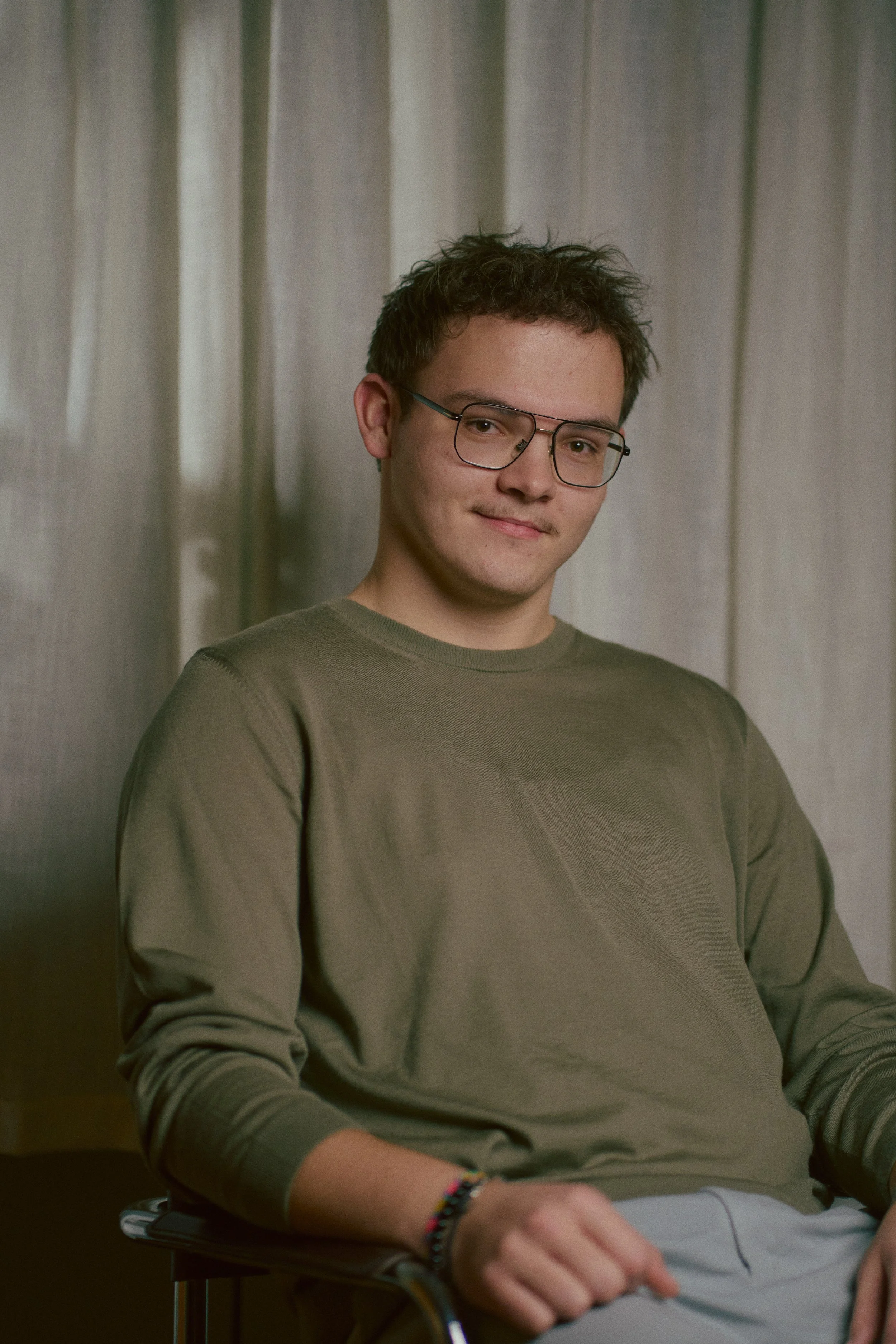 Ein junger Mann mit Brille sitzt lächelnd vor einem neutralen Hintergrund.