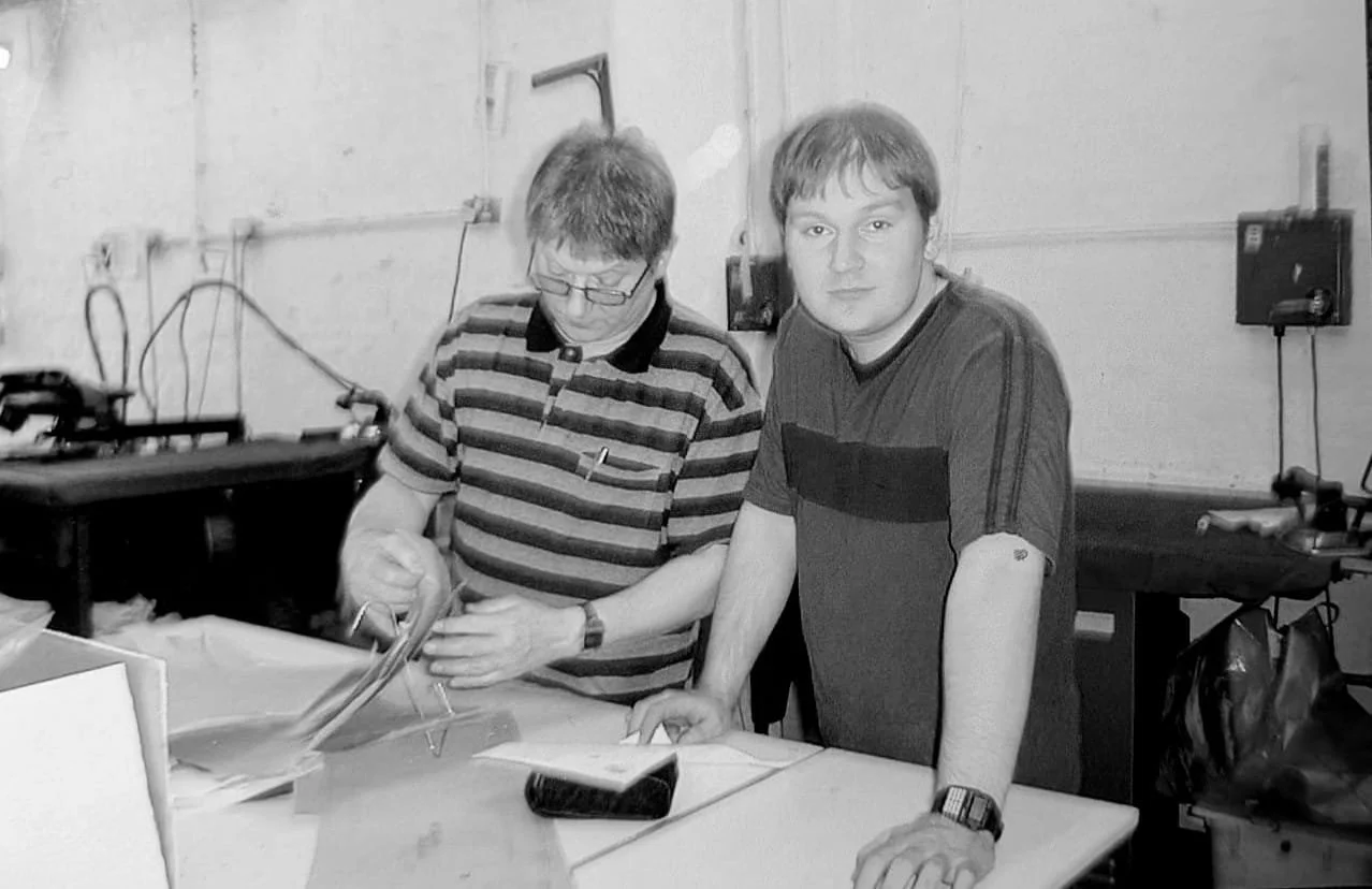 Two young men in a room with electronic equipment and papers on a table.