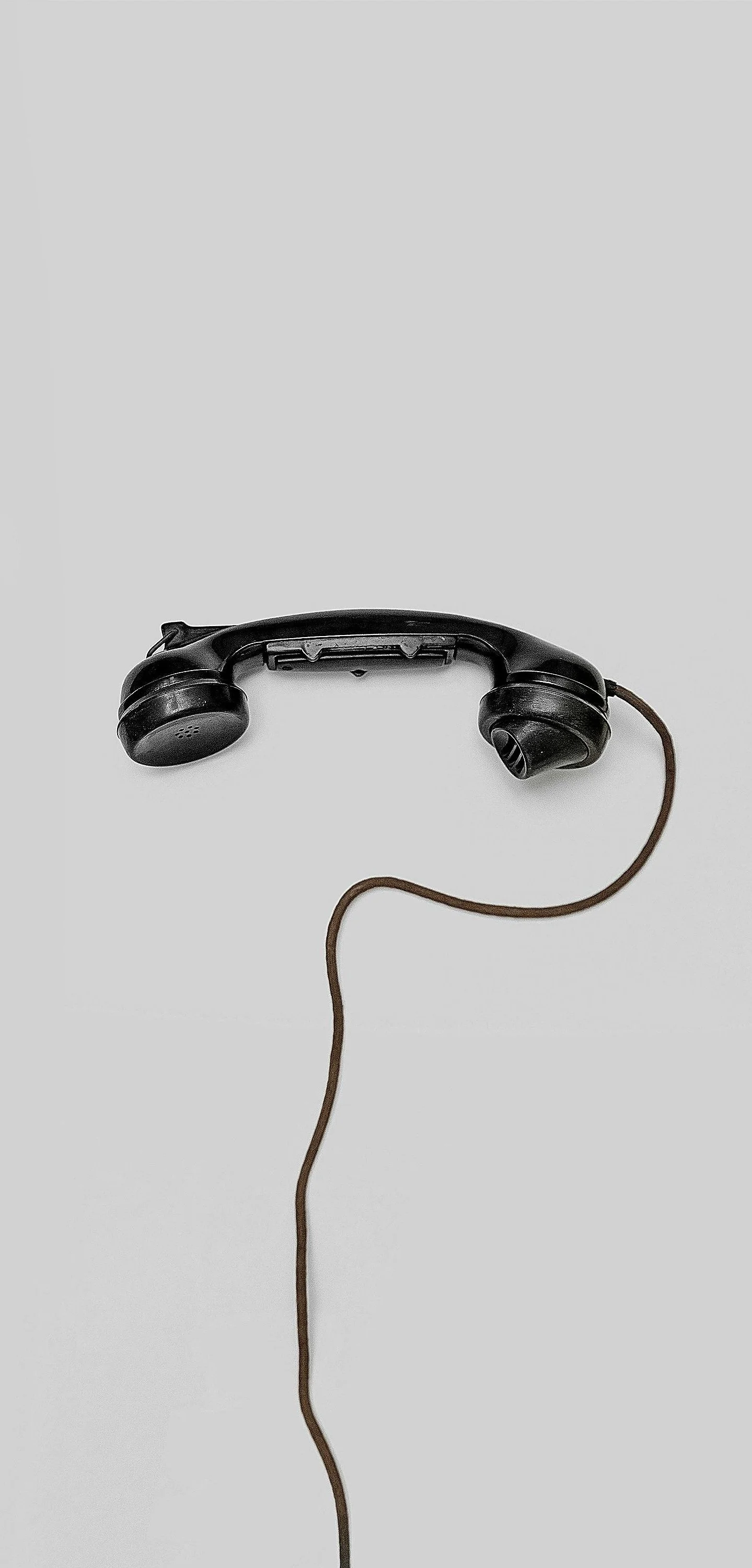 Old black telephone handset with cord on a plain white surface.