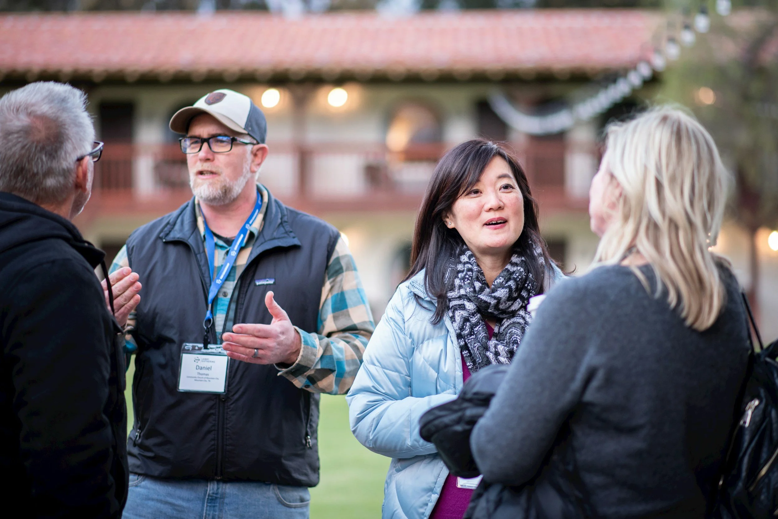 Four people engaged in conversation outdoors at what appears to be a social or networking event, with a house or lodge in the background.