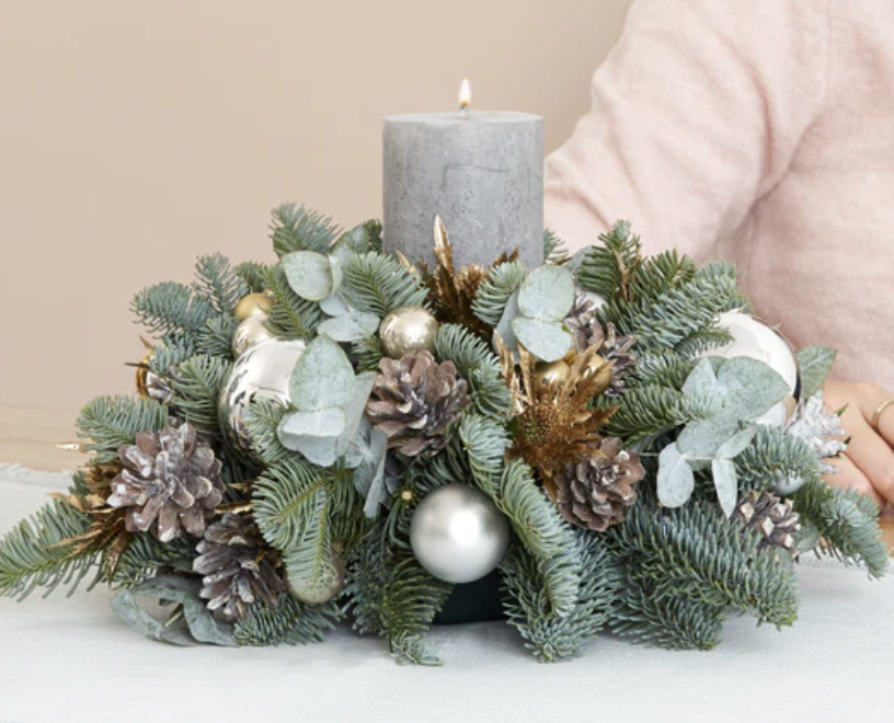 Festive Christmas centerpiece with greenery, pinecones, baubles, and a gray candle.