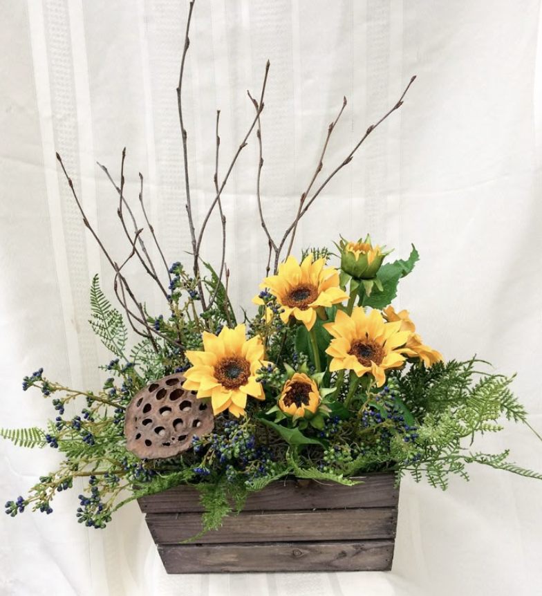 A wooden rectangular planter filled with yellow sunflowers, greenery, purple berries, and tall leafless branches.