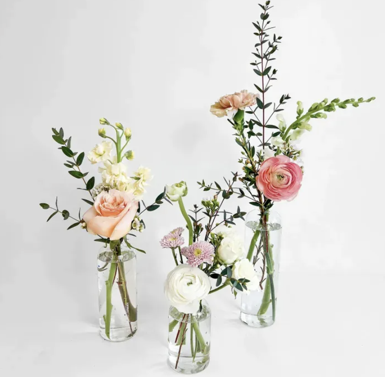 Three vases with assorted flowers and greenery on a white background.