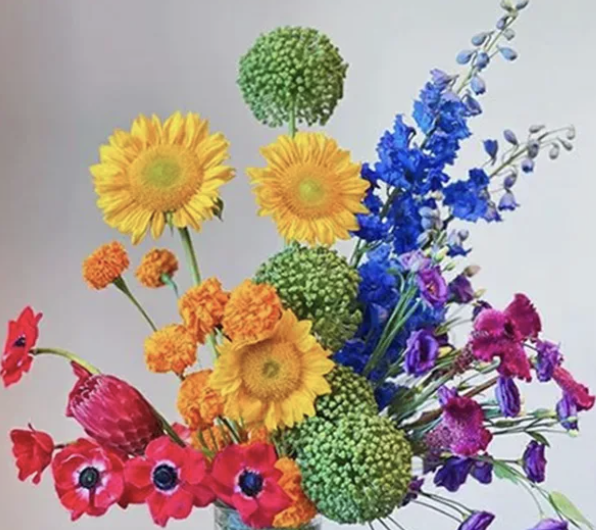 Colorful mixed flower bouquet including sunflowers, green pom-pom flowers, orange marigolds, pink poppies, purple and blue delphiniums, and other seasonal flowers.