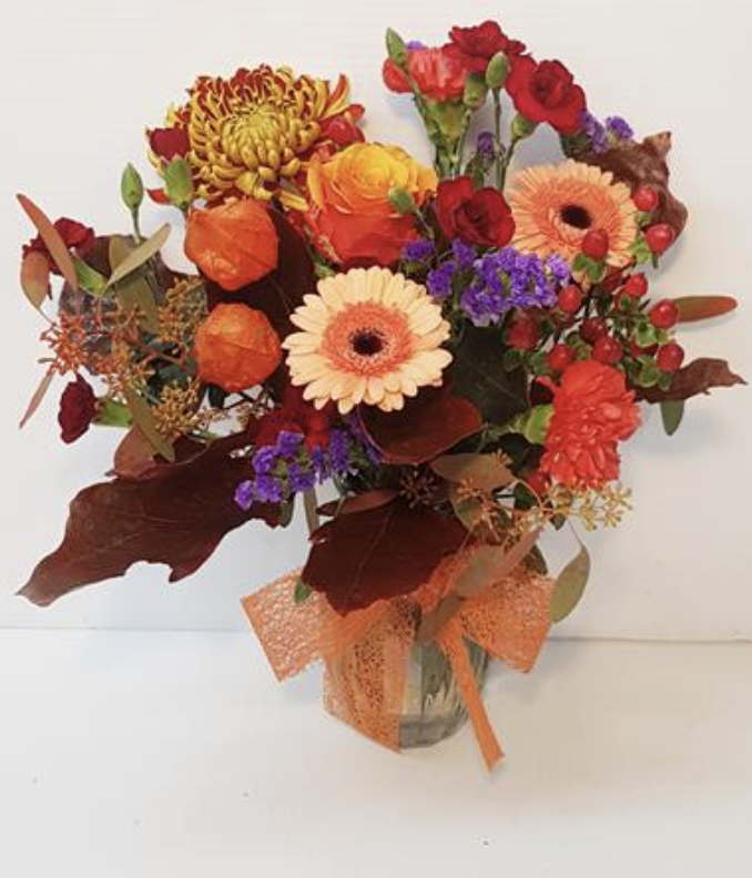 A colorful bouquet of flowers in a glass vase, tied with orange netted ribbon.