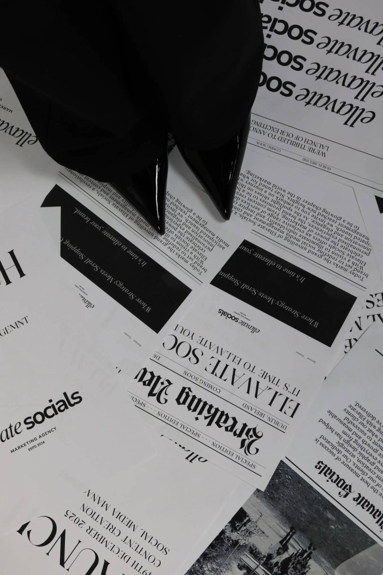 Close-up of a black pointed-toe shoe placed on scattered black-and-white event tickets or flyers, with some text visible.