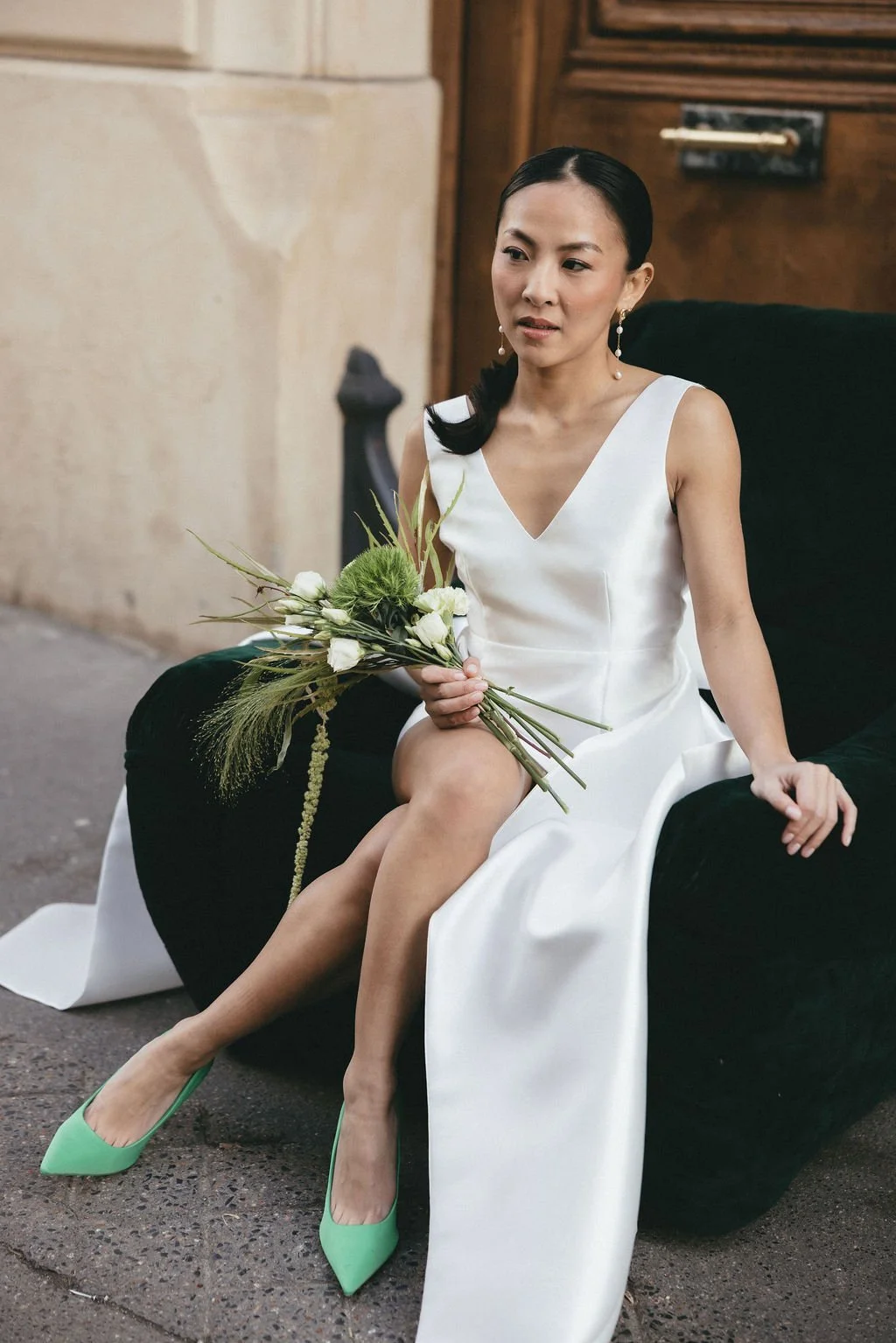 Mariée assise tenant un bouquet vert, moment joyeux et spontané en ville.