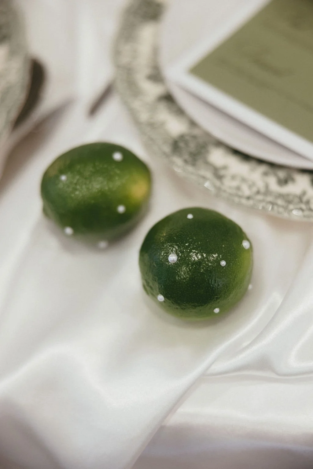 Citrons verts posés sur tissu satiné, détail frais et végétal pour une décoration de mariage élégante.