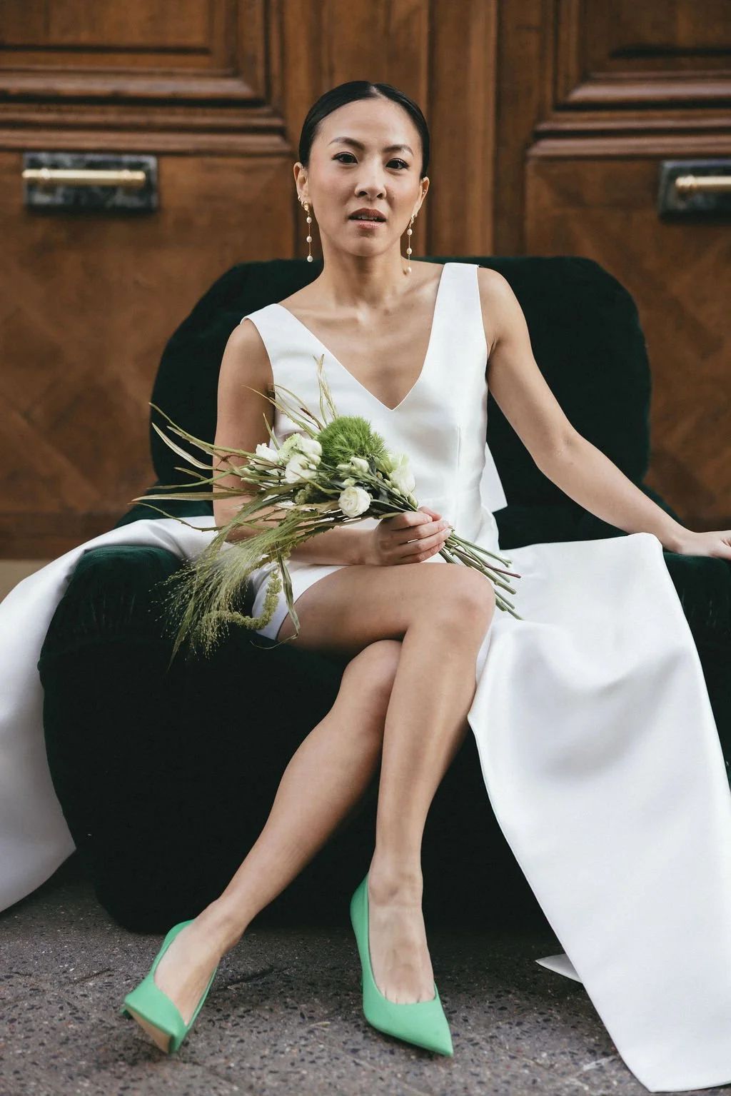 Mariée assise tenant un bouquet vert, moment joyeux et spontané en ville.