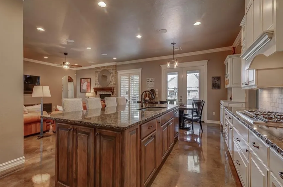 Open-concept kitchen and living room area with a large center island, white cabinets, hardwood floors, a fireplace, and a dining area with a glass door leading outside.