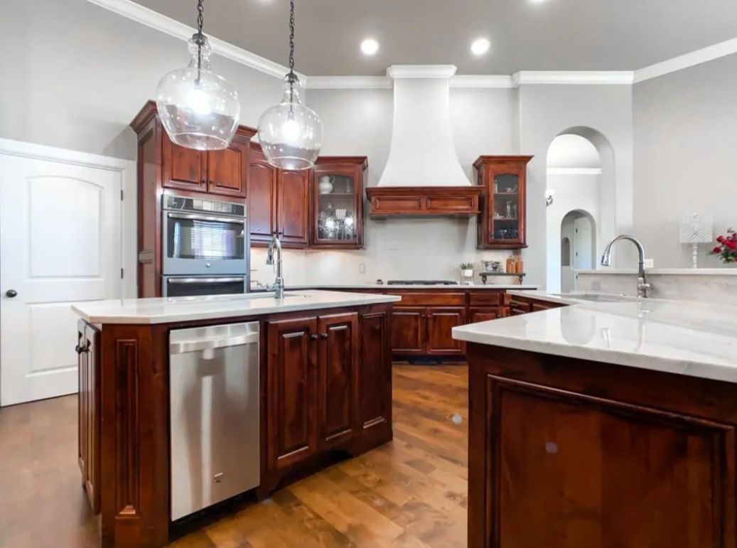 Modern kitchen with wooden cabinets, white countertops, two glass pendant lights, stainless steel appliances, and an arched doorway.