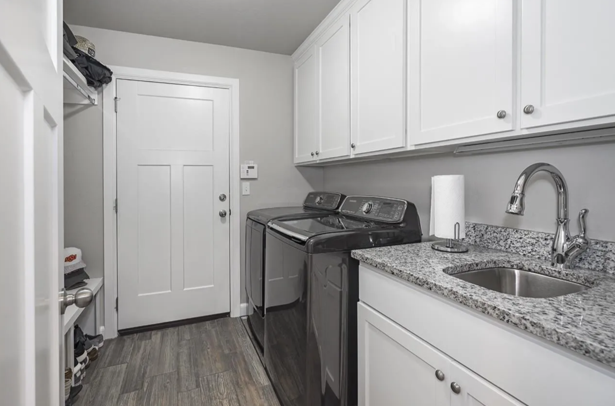 Laundry room with white cabinets, a granite countertop, a stainless steel sink, a roll of paper towels, a black washing machine, and a white door.