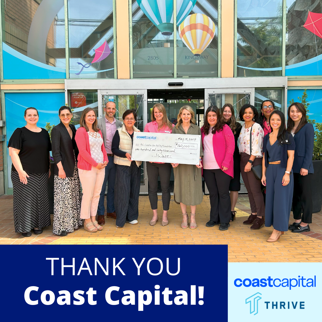 A group of people standing outside a building, holding a large check for $160,000 from Coast Capital, celebrating a donation or grant. The building has colorful kites and hot air balloons decorations on the windows.